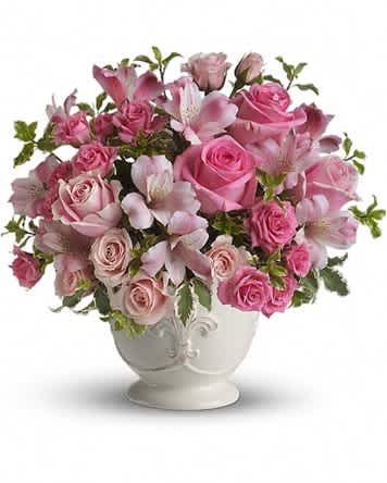 Pink roses and lilies arranged in a white urn vase