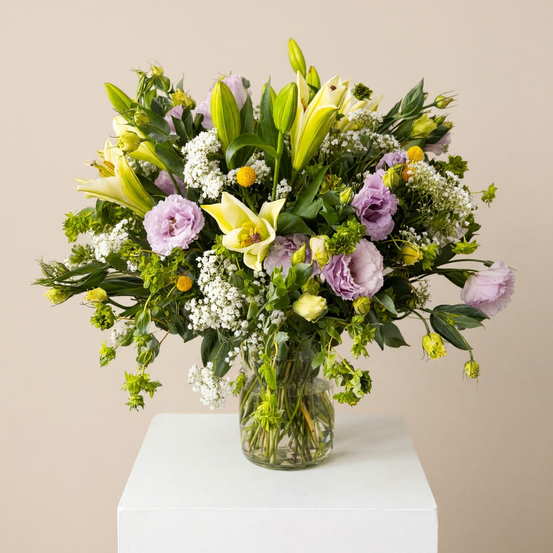 Bouquet of pale yellow lilies and lavender flowers in a glass vase