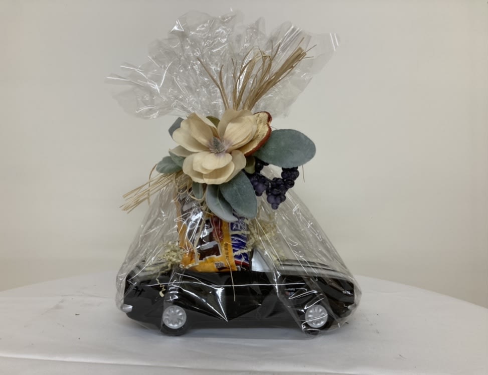 Gift basket wrapped in clear cellophane with flowers and snacks on a black tray