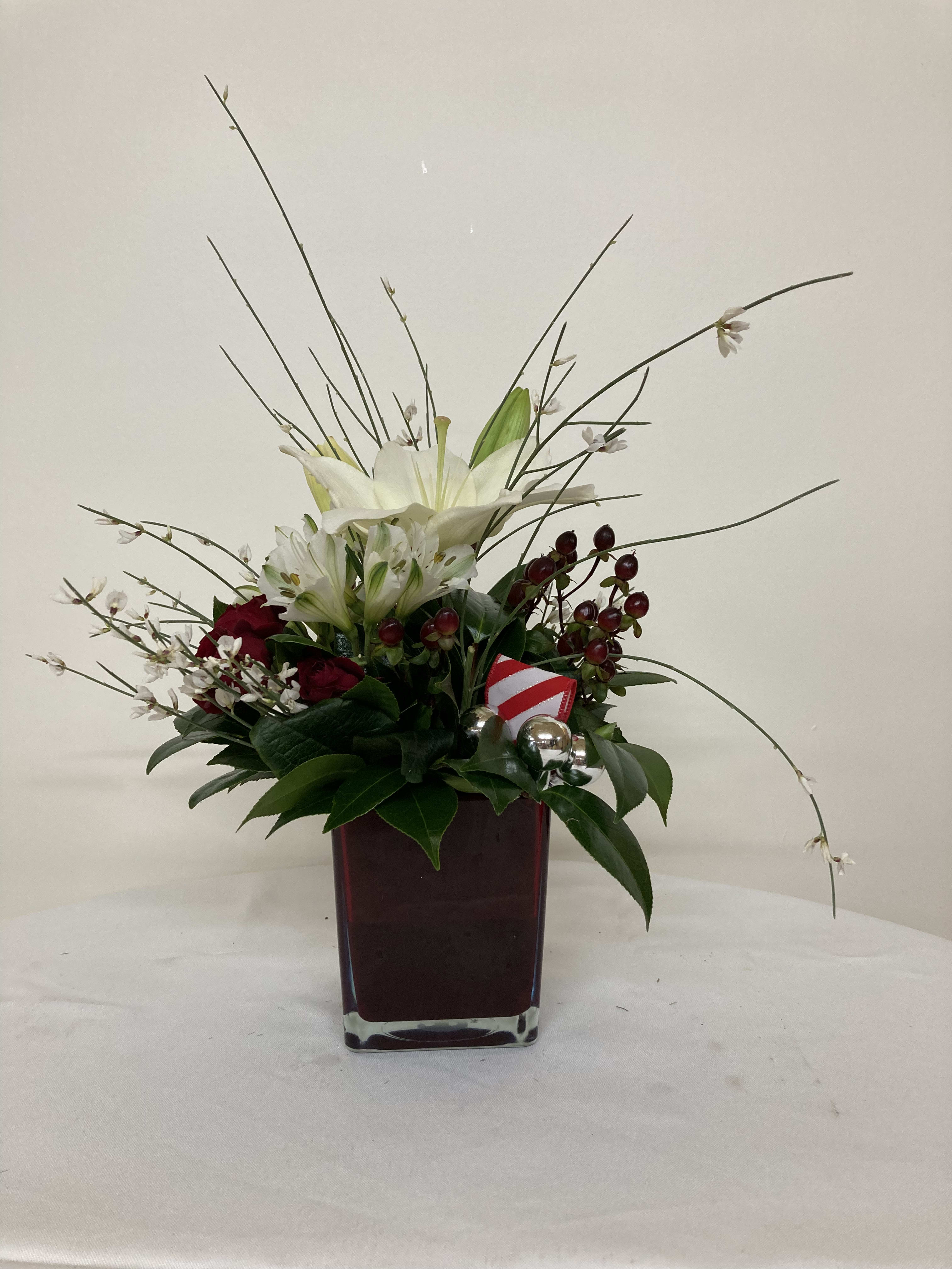 White lilies and red roses in a square glass vase with holiday accents