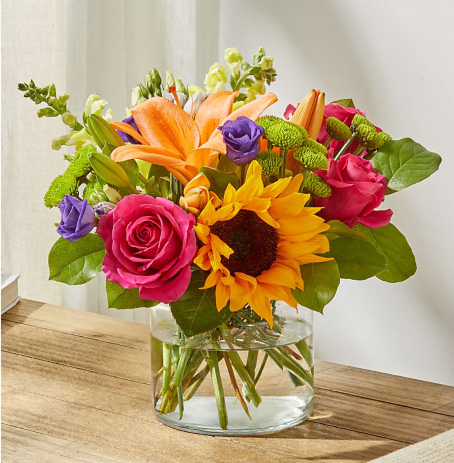 Bright mixed bouquet with sunflowers, roses, lilies, and a glass vase