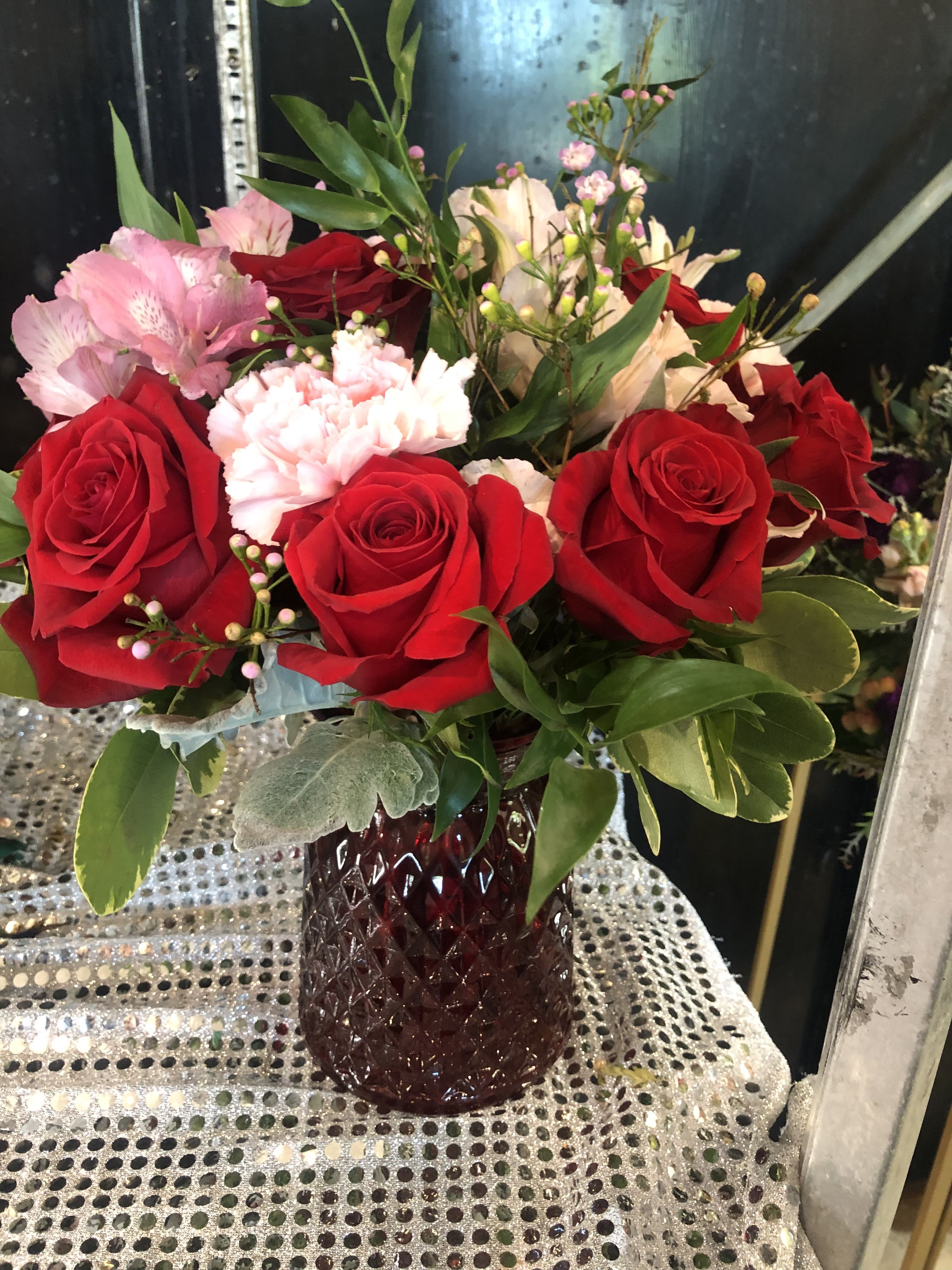 Bouquet of red roses, pink alstroemeria, and white carnations in a red vase