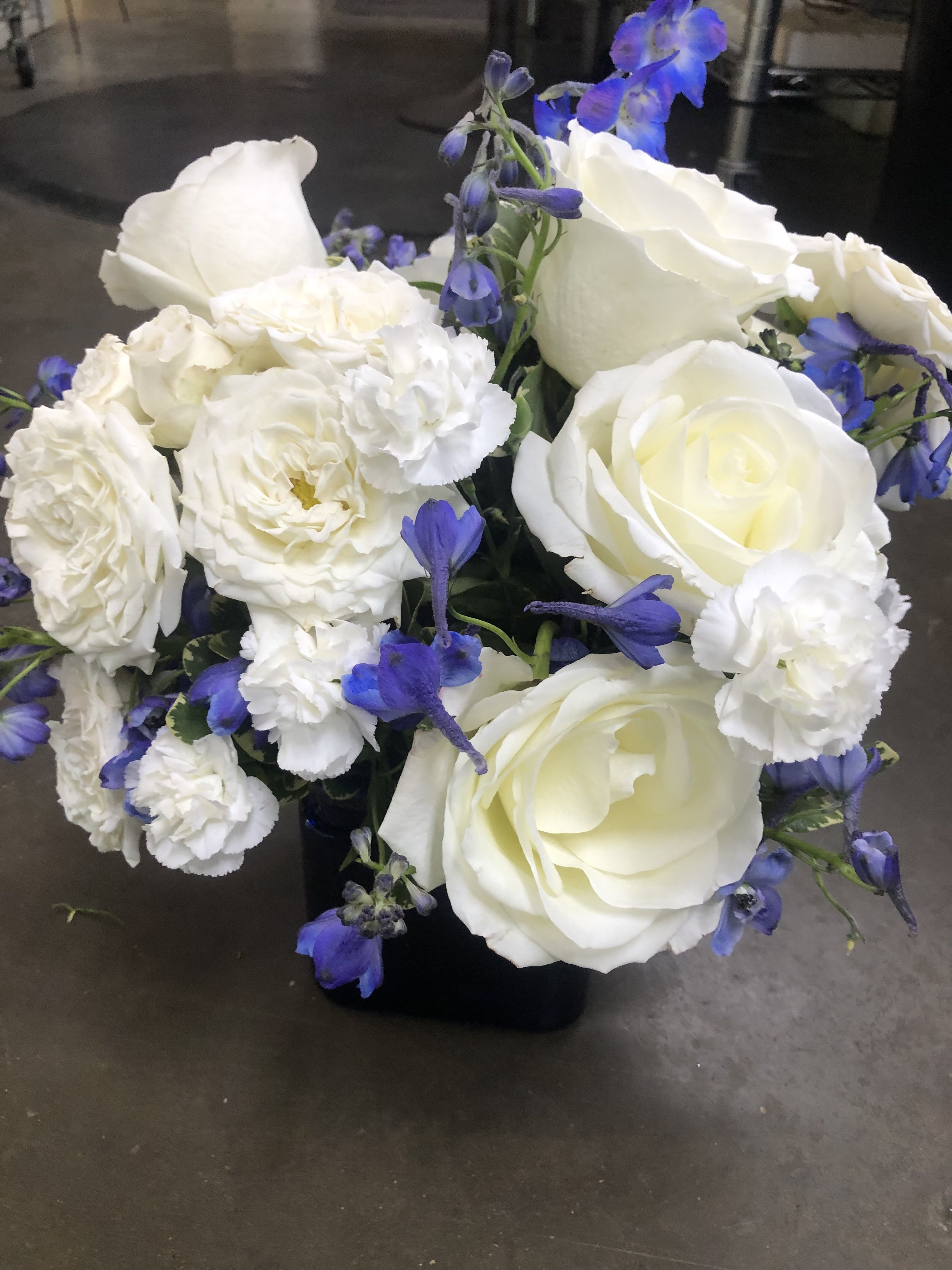 White roses and carnations with blue accents in a black vase