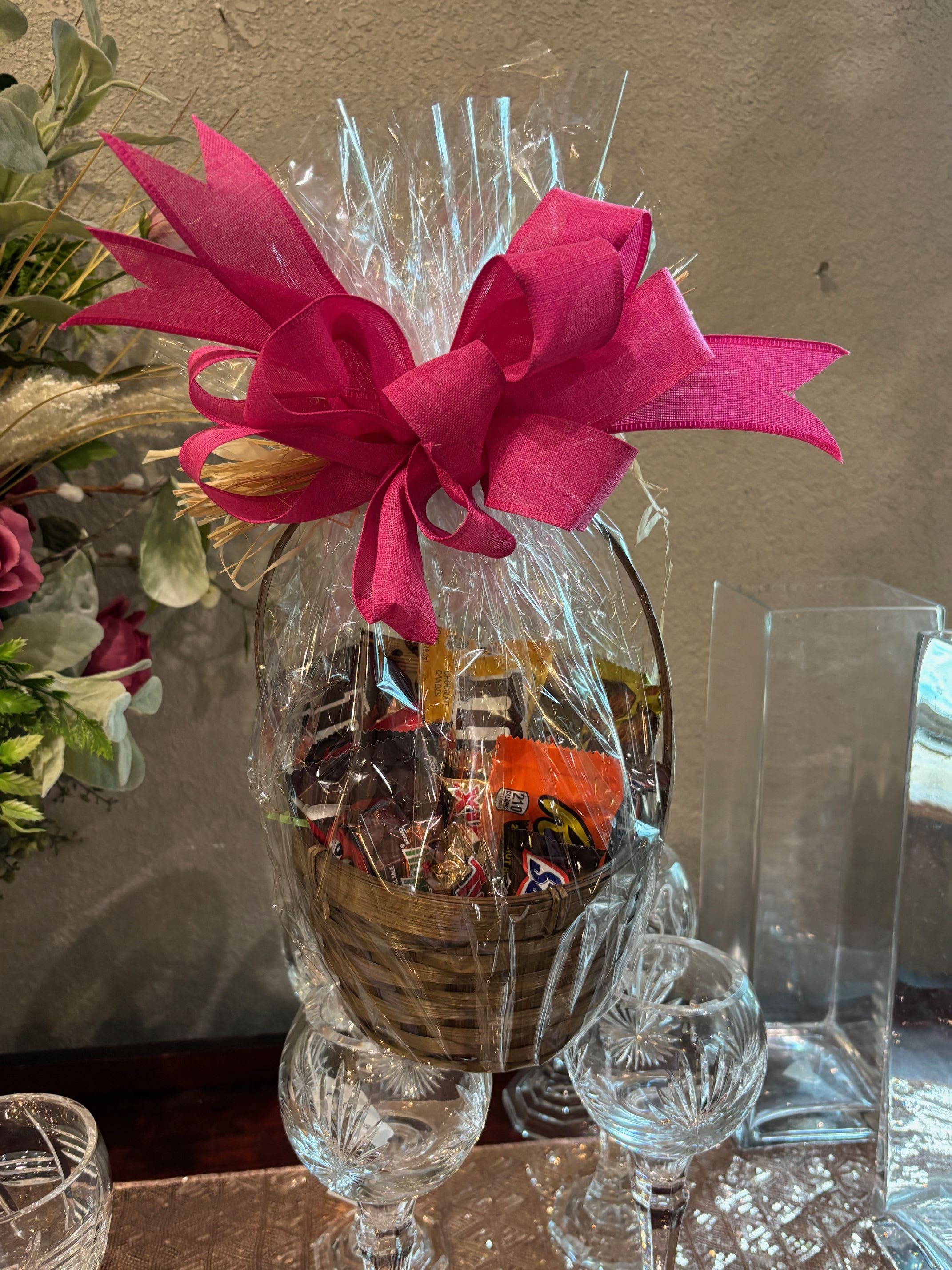 Basket of assorted chocolates wrapped in clear cellophane with a bright pink bow