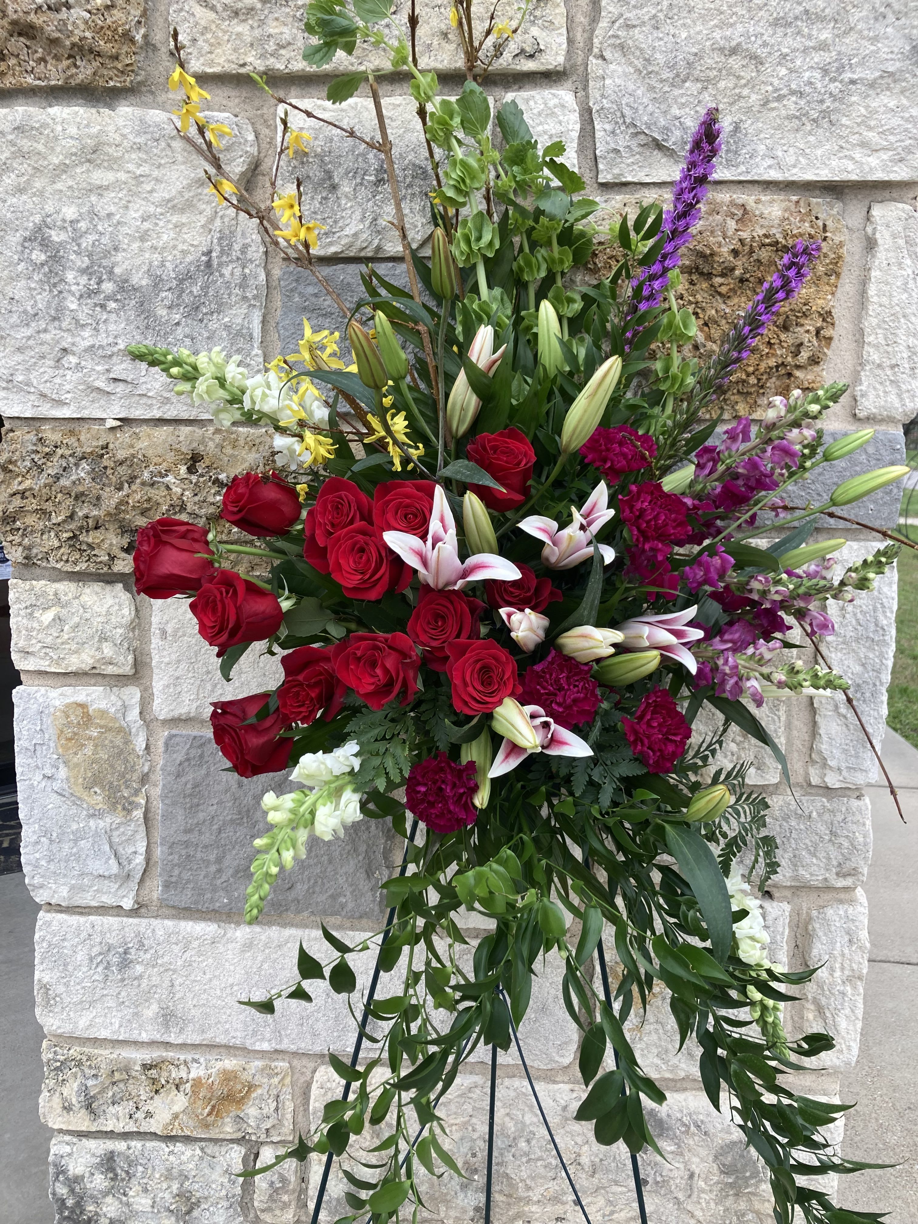 Tall standing floral spray with red roses, lilies, and purple accents