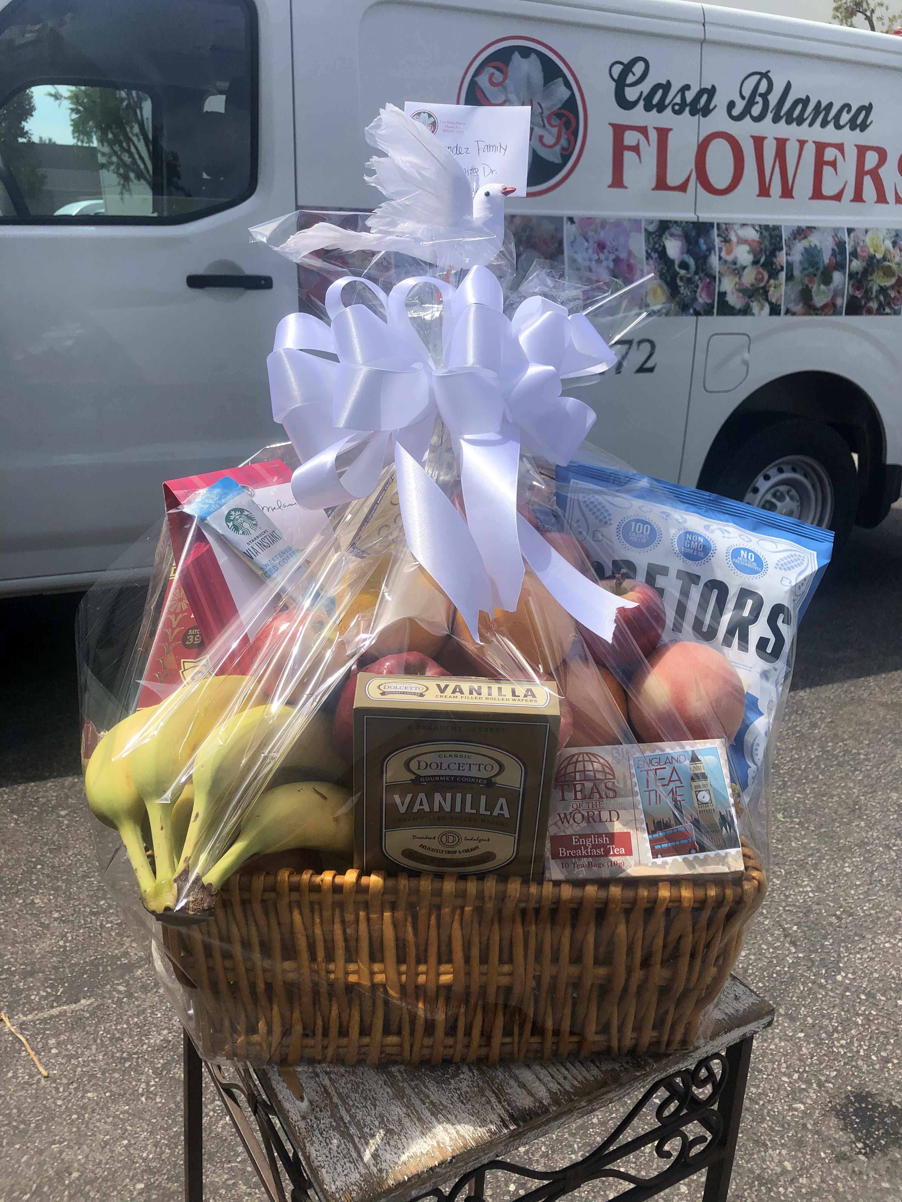 Gift basket with fruit, cookies, tea, and a white ribbon bow