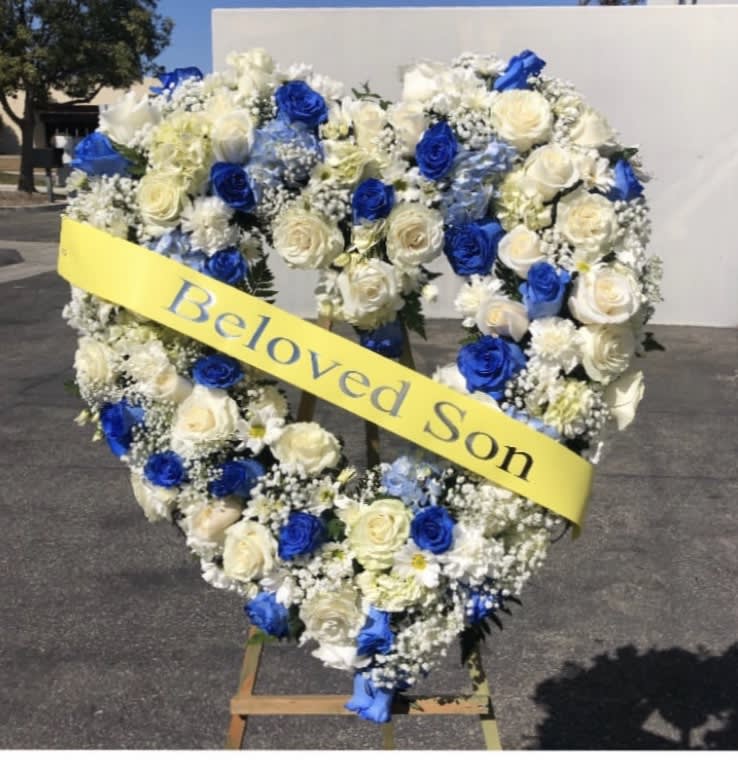 Heart-shaped floral wreath with blue and white roses and a yellow ribbon