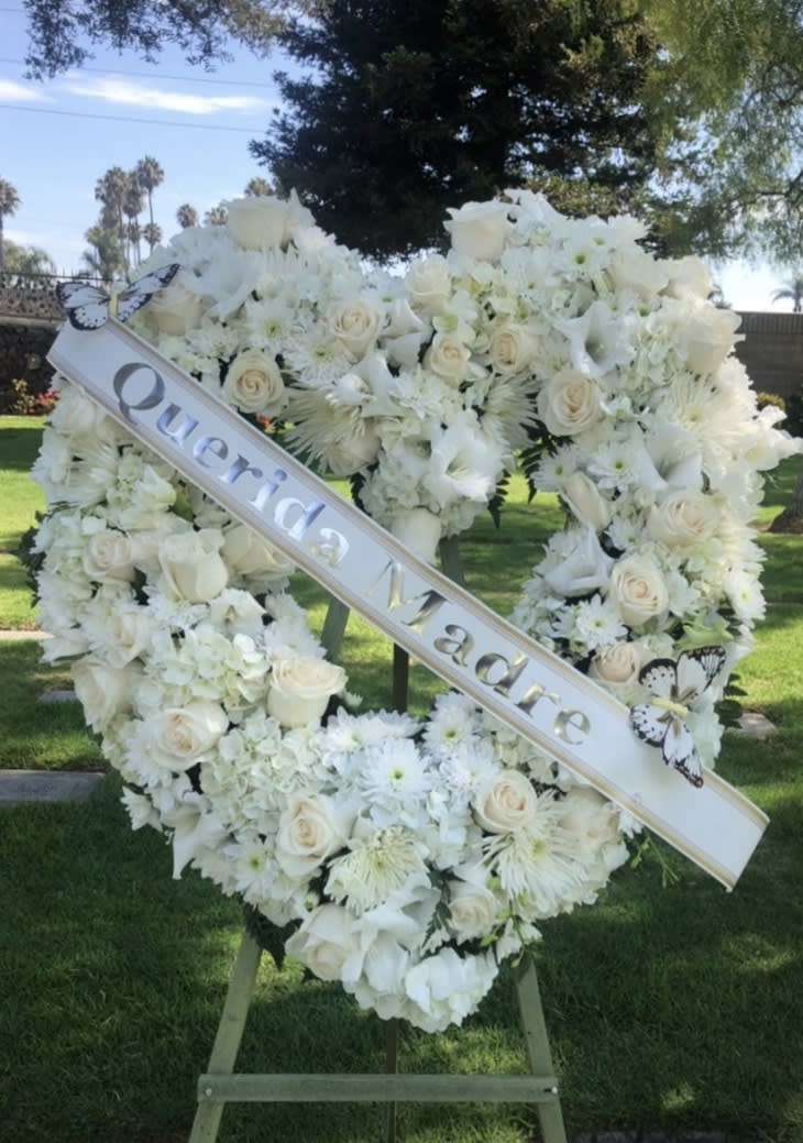 White floral funeral wreath on an easel with a diagonal memorial ribbon