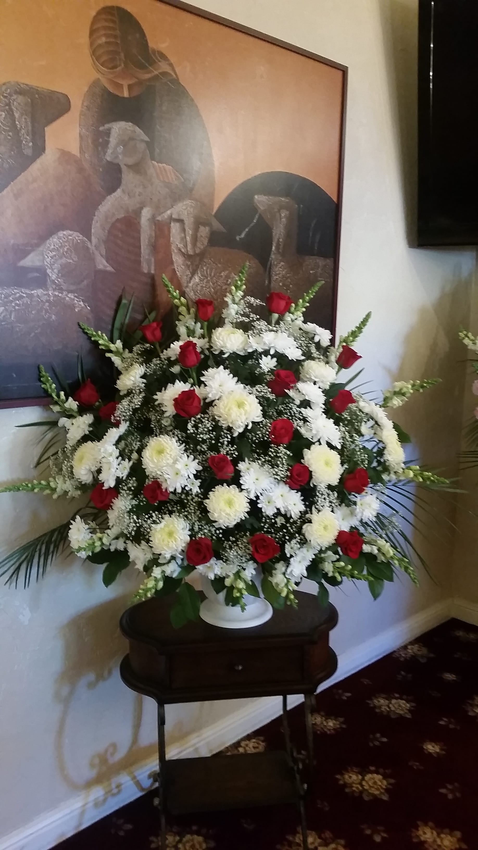 Large standing arrangement of red roses and white chrysanthemums in a white urn
