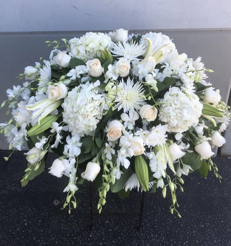 White floral casket spray with roses, lilies, and hydrangeas