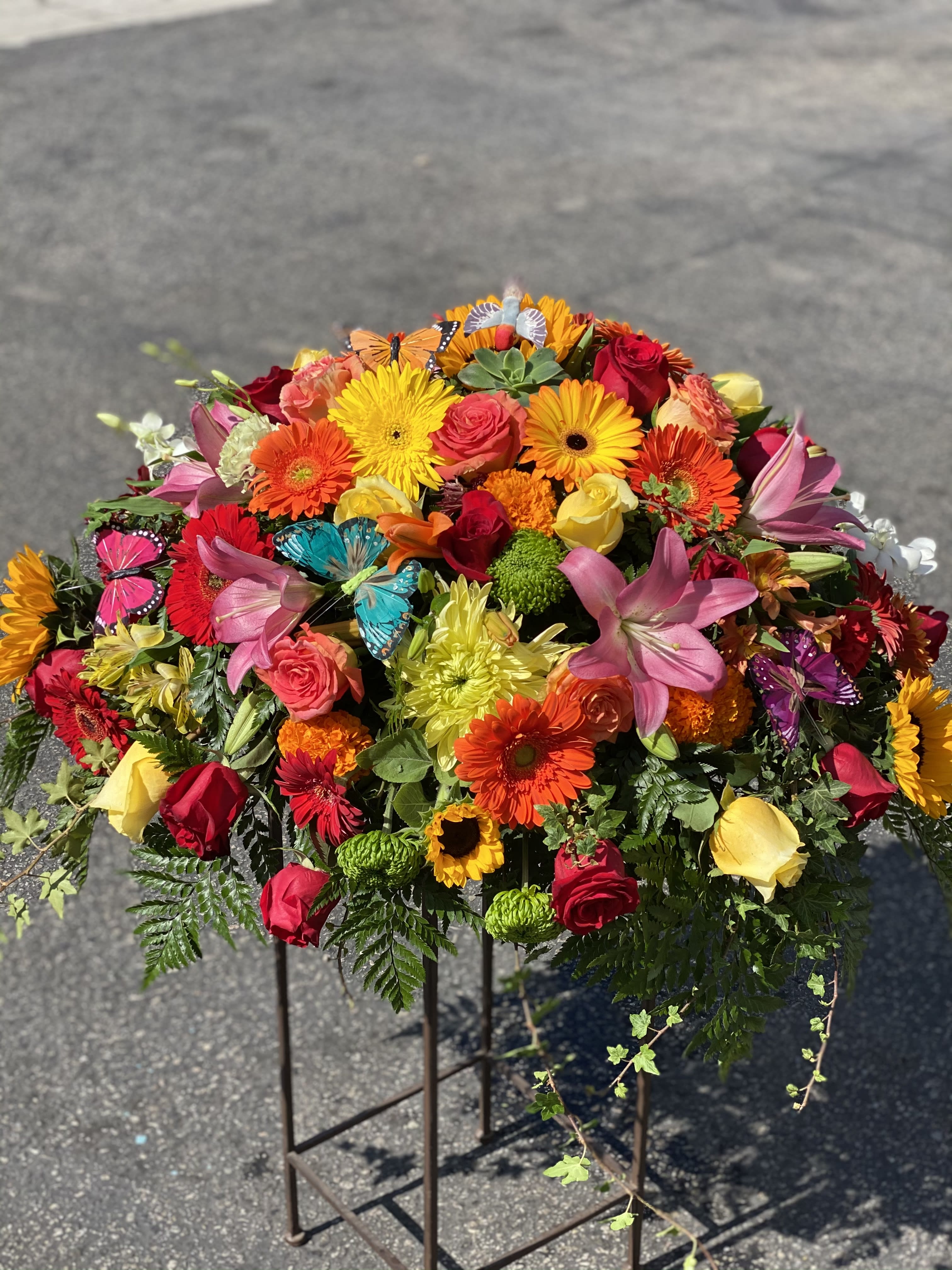 Colorful mixed flower arrangement on a stand with roses, gerbera daisies, lilies, and butterflies