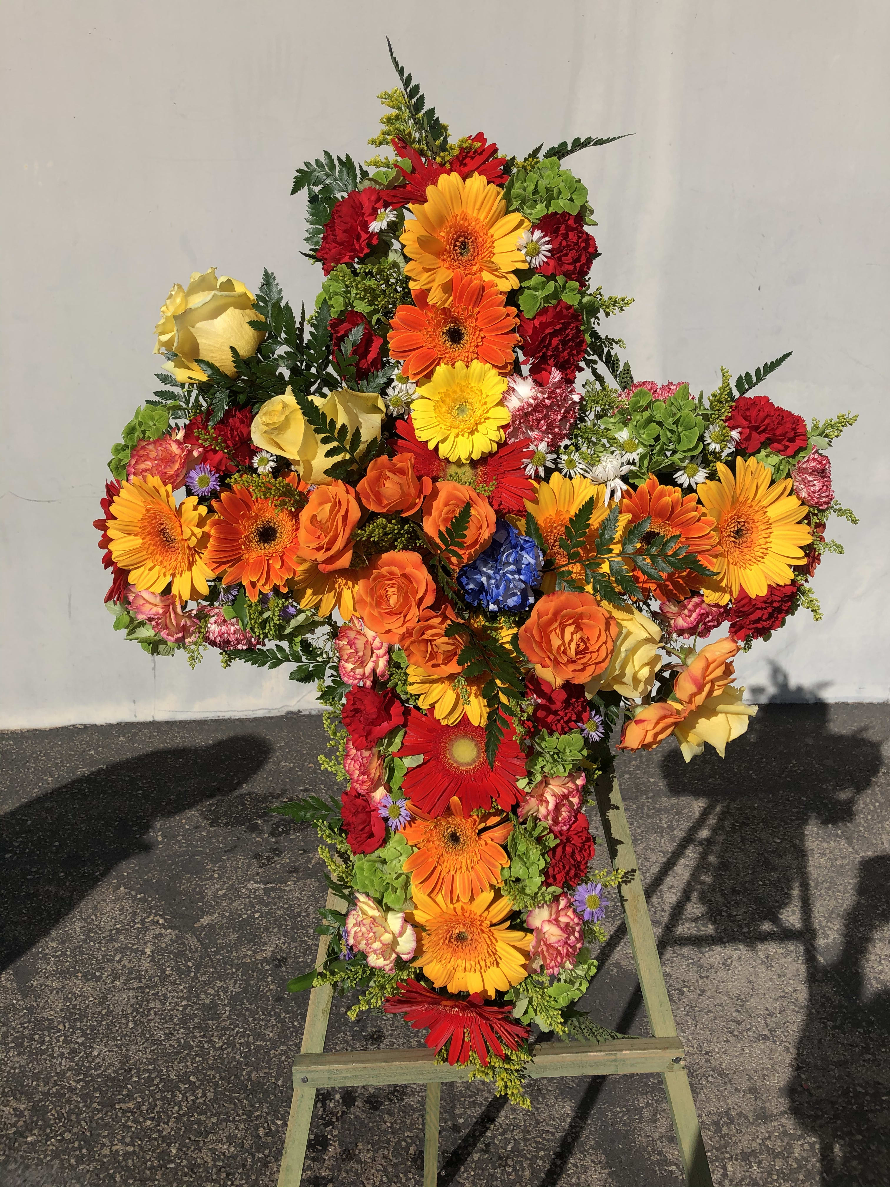 Cross-shaped floral spray with bright mixed blooms on a stand