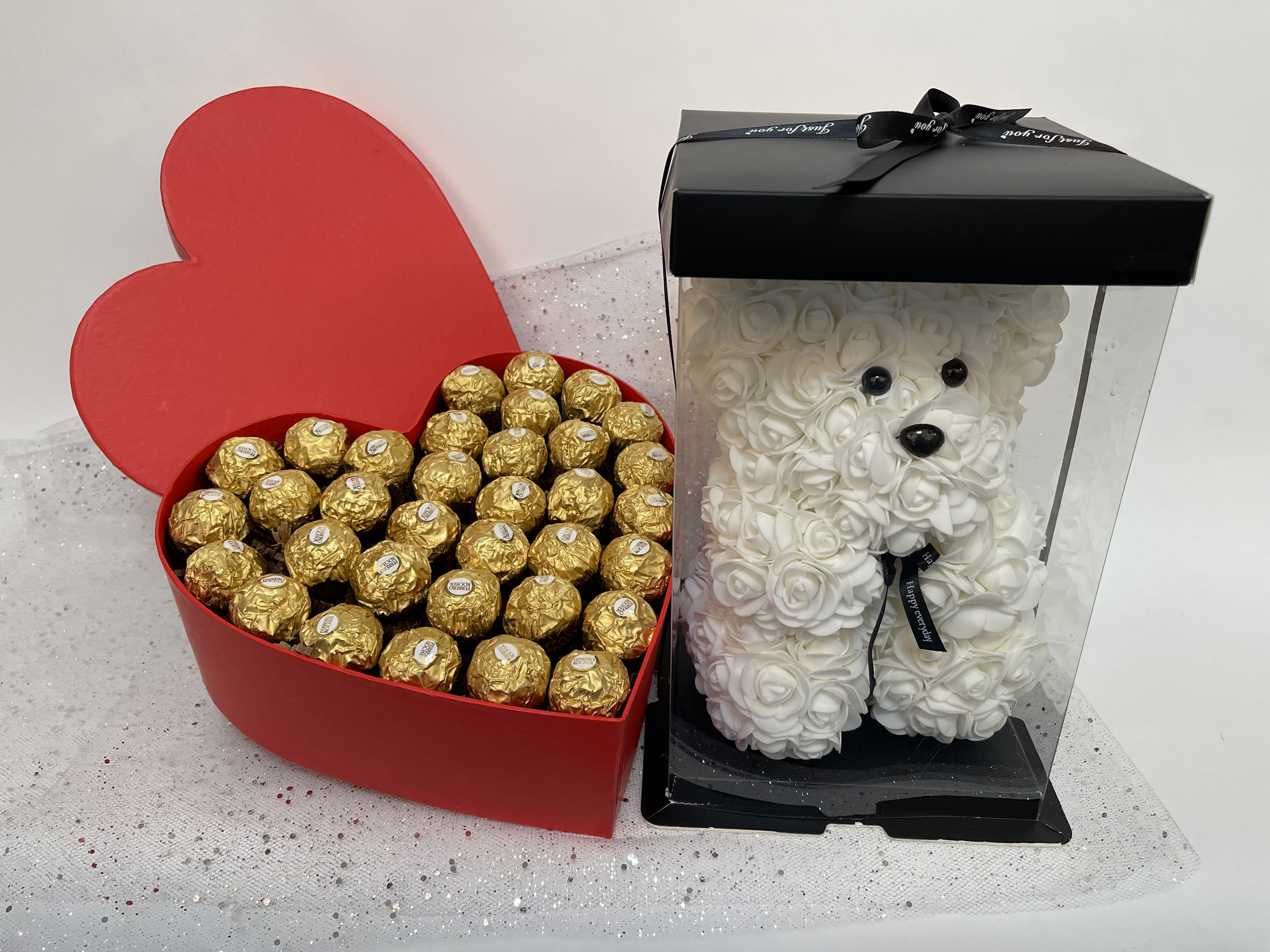 Heart-shaped candy box and a white rose teddy bear in a display case
