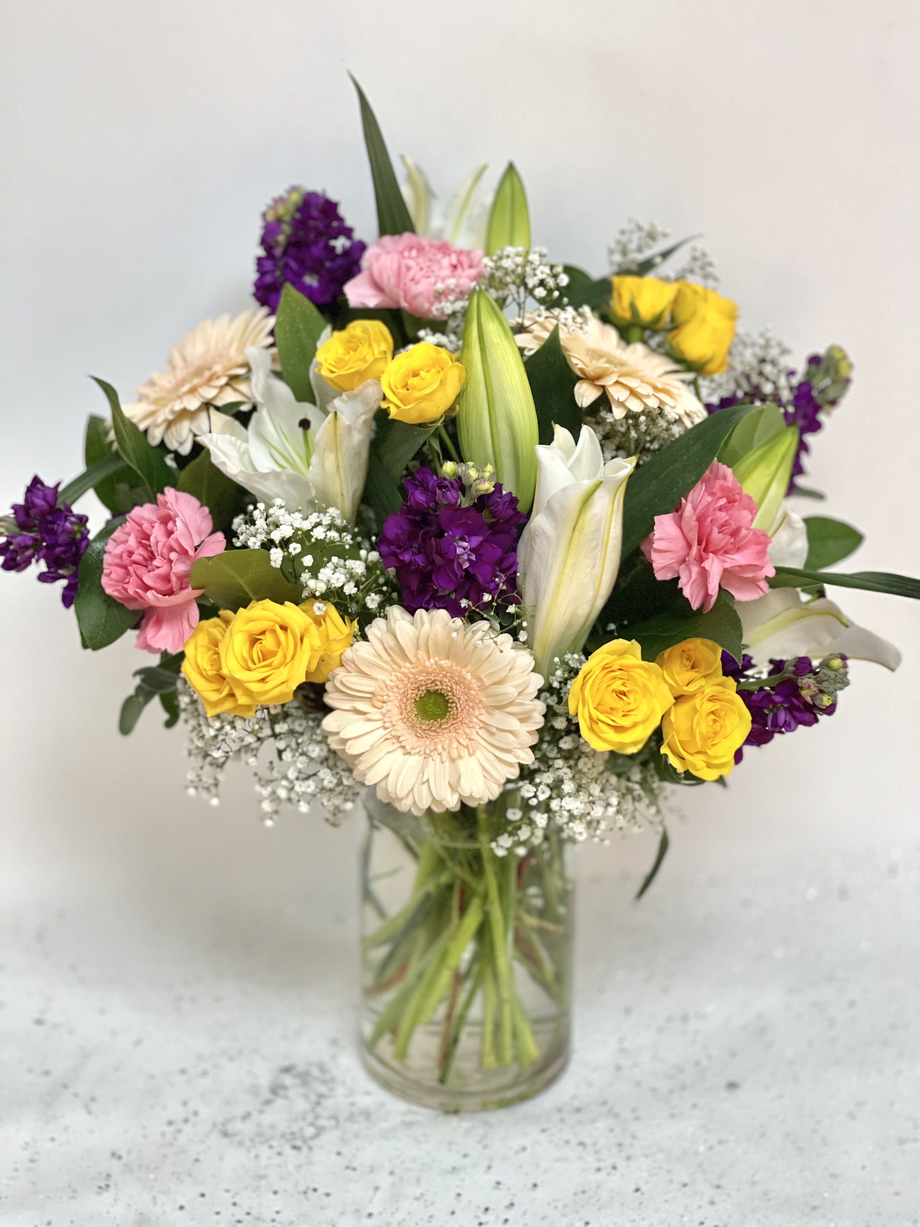 Mixed bouquet of yellow roses, pink carnations, lilies, and daisies in a glass vase