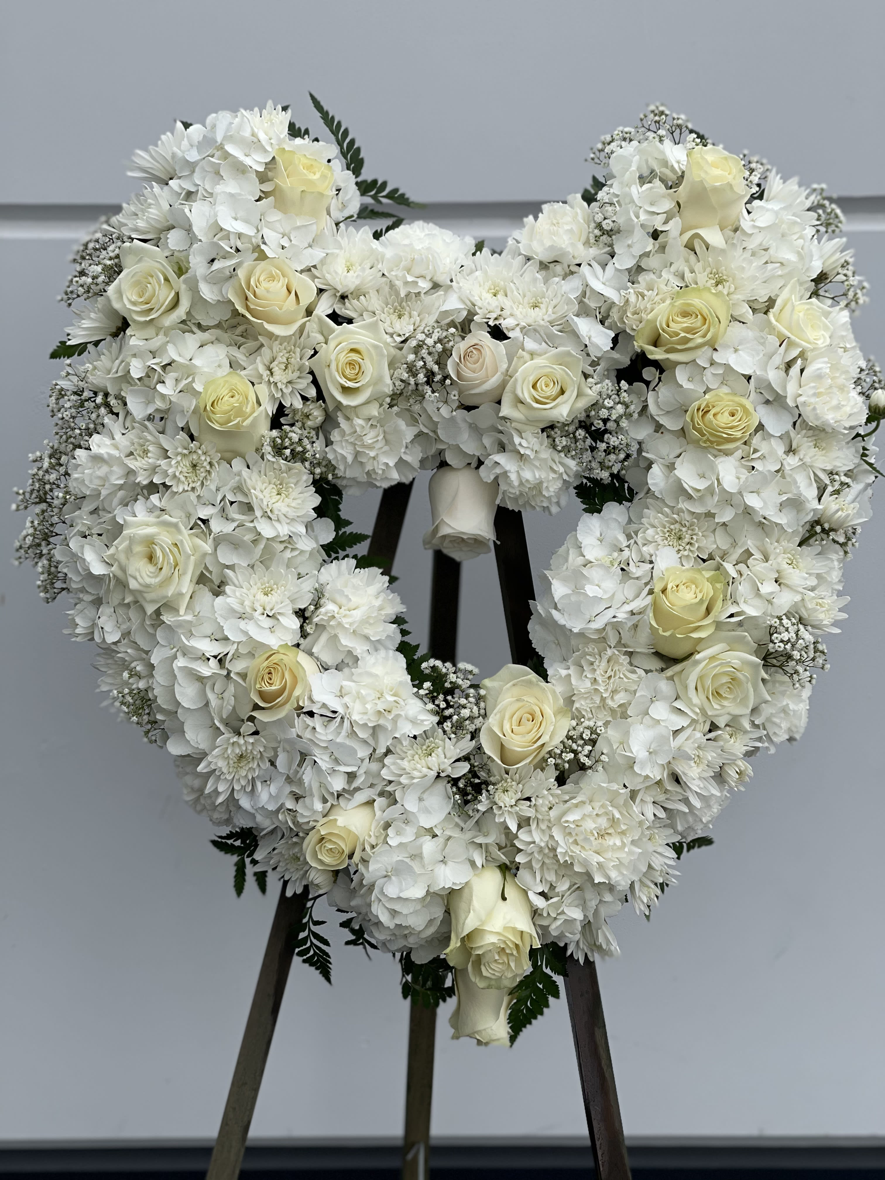 Heart-shaped white floral wreath with cream roses on a stand