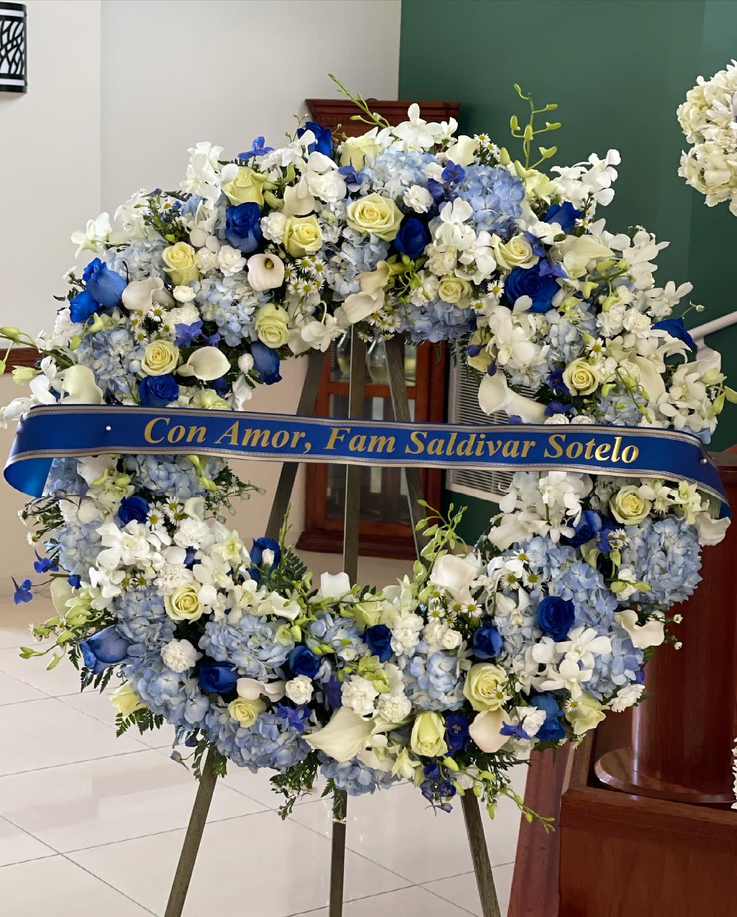 Large blue and white floral wreath on an easel with a memorial ribbon
