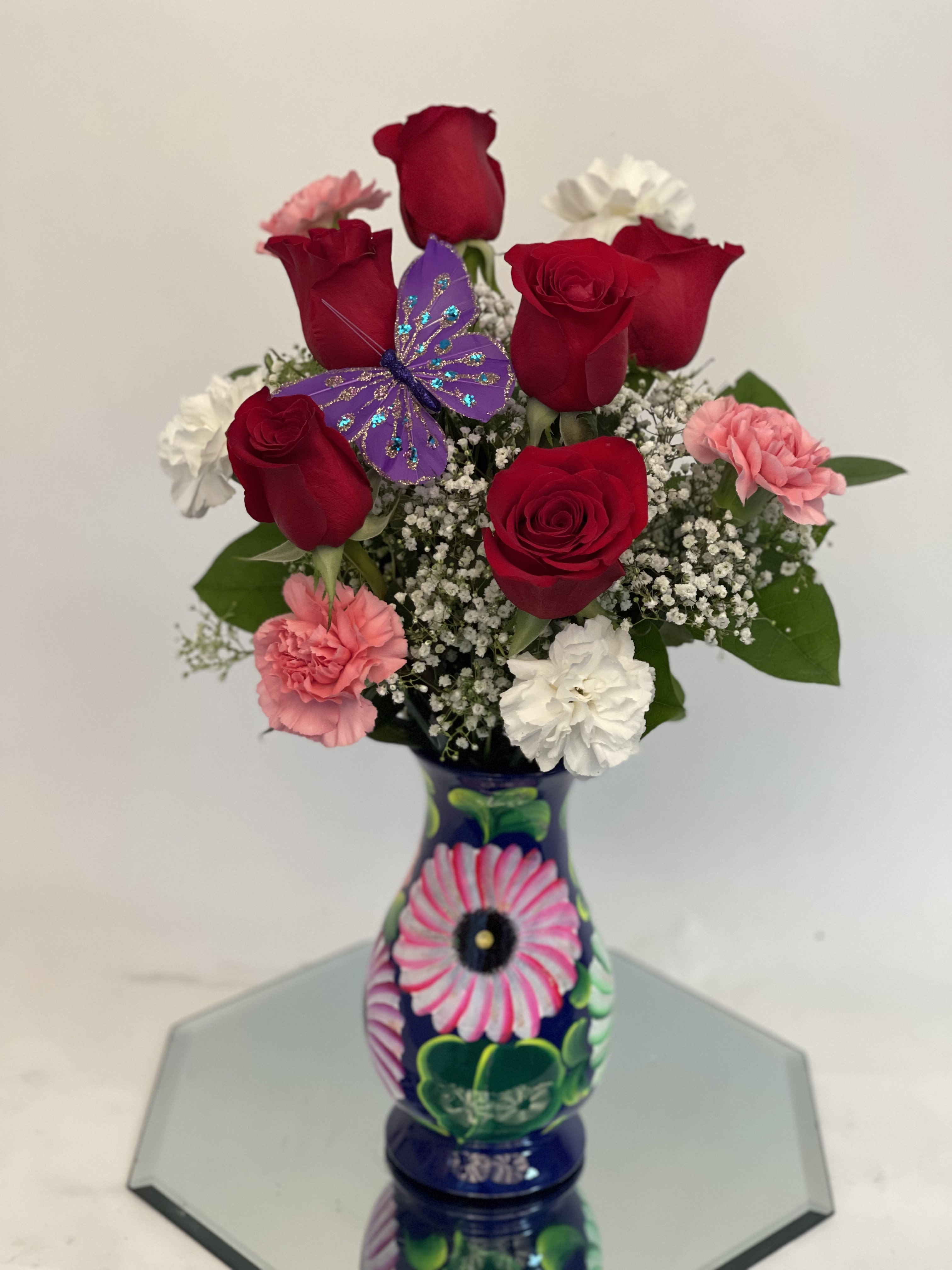 Red roses and pink carnations in a painted vase with a purple butterfly decoration
