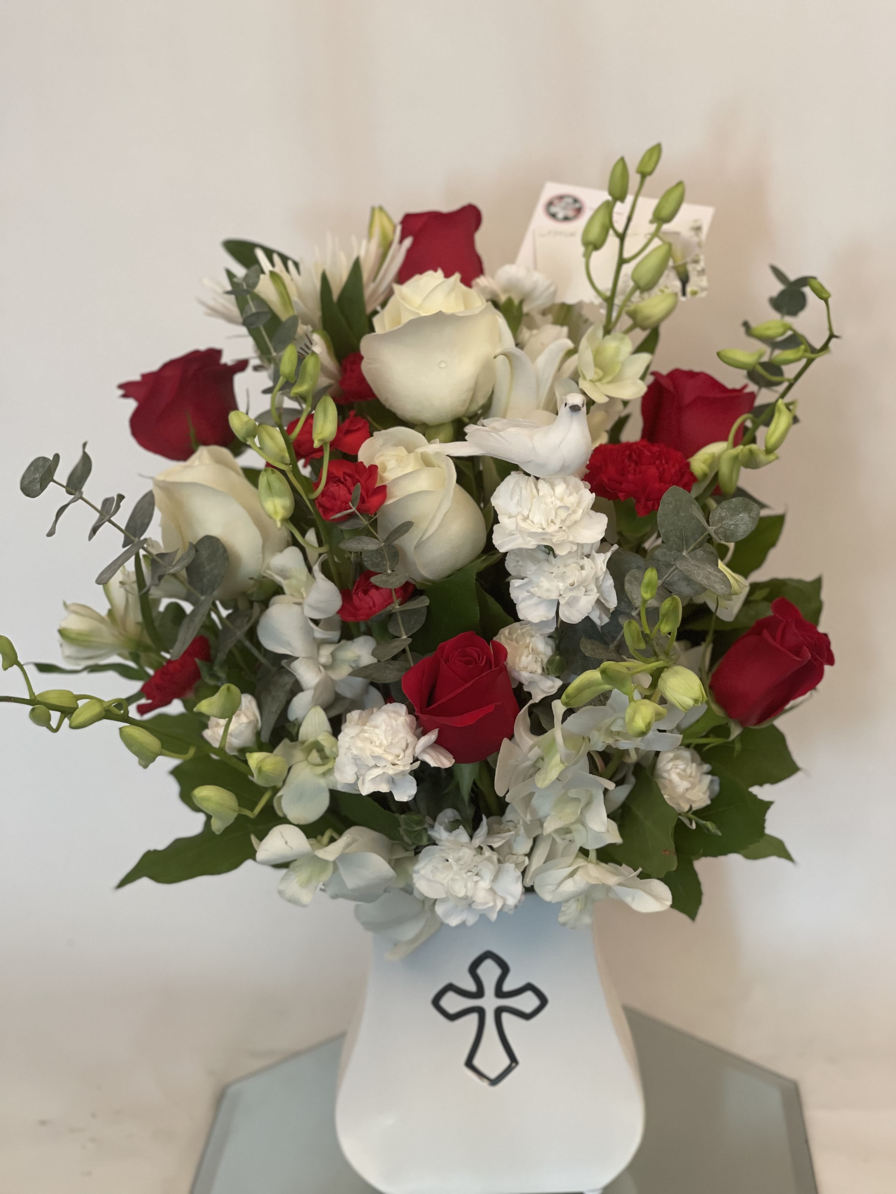 Red and white flower arrangement in a white vase with a cross emblem