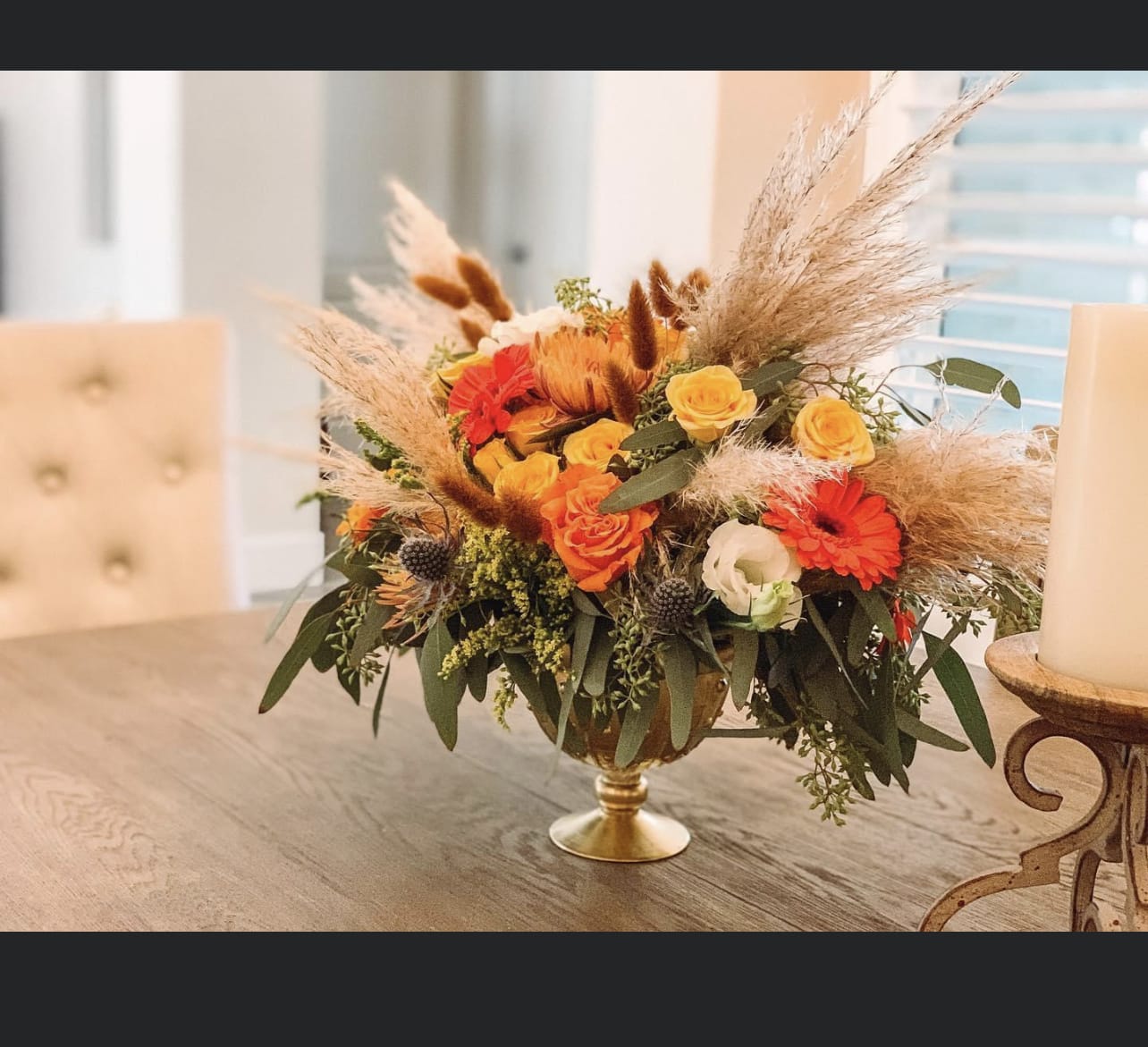 Orange and yellow flower arrangement in a gold pedestal bowl