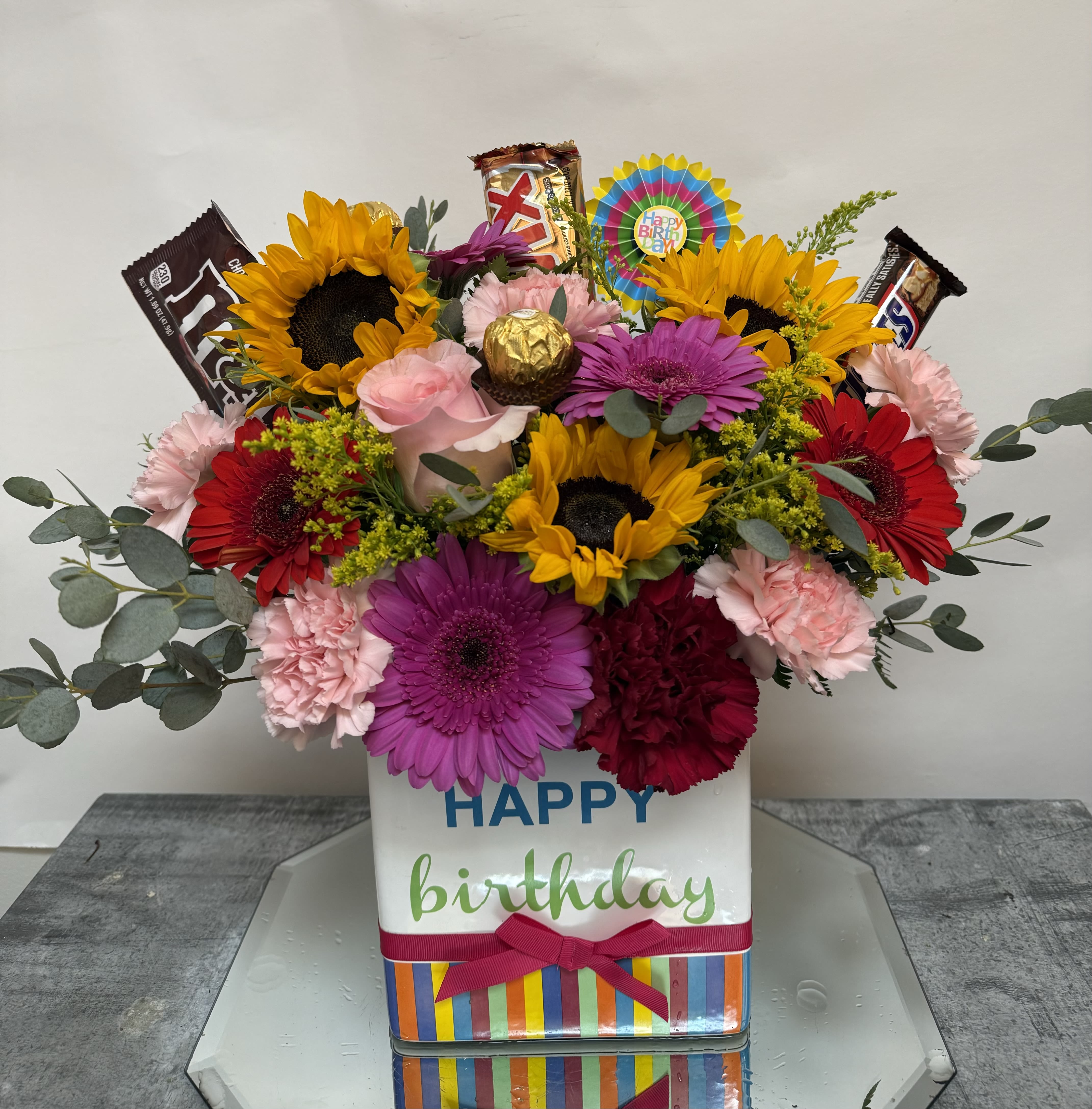 Birthday flower arrangement with sunflowers, gerberas, carnations, and candy bars in a gift box