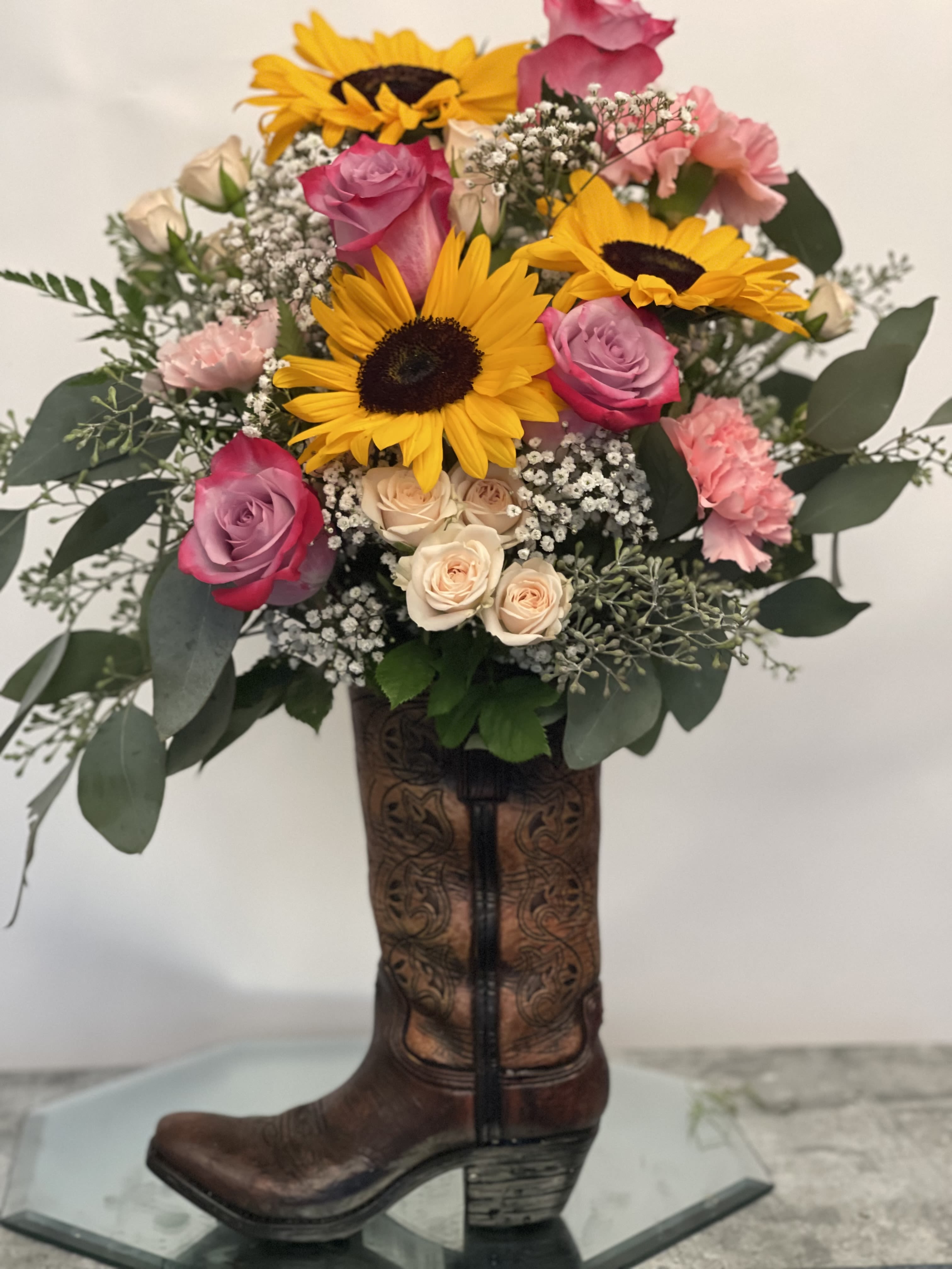 Bouquet of sunflowers, pink roses, and carnations in a cowboy boot vase