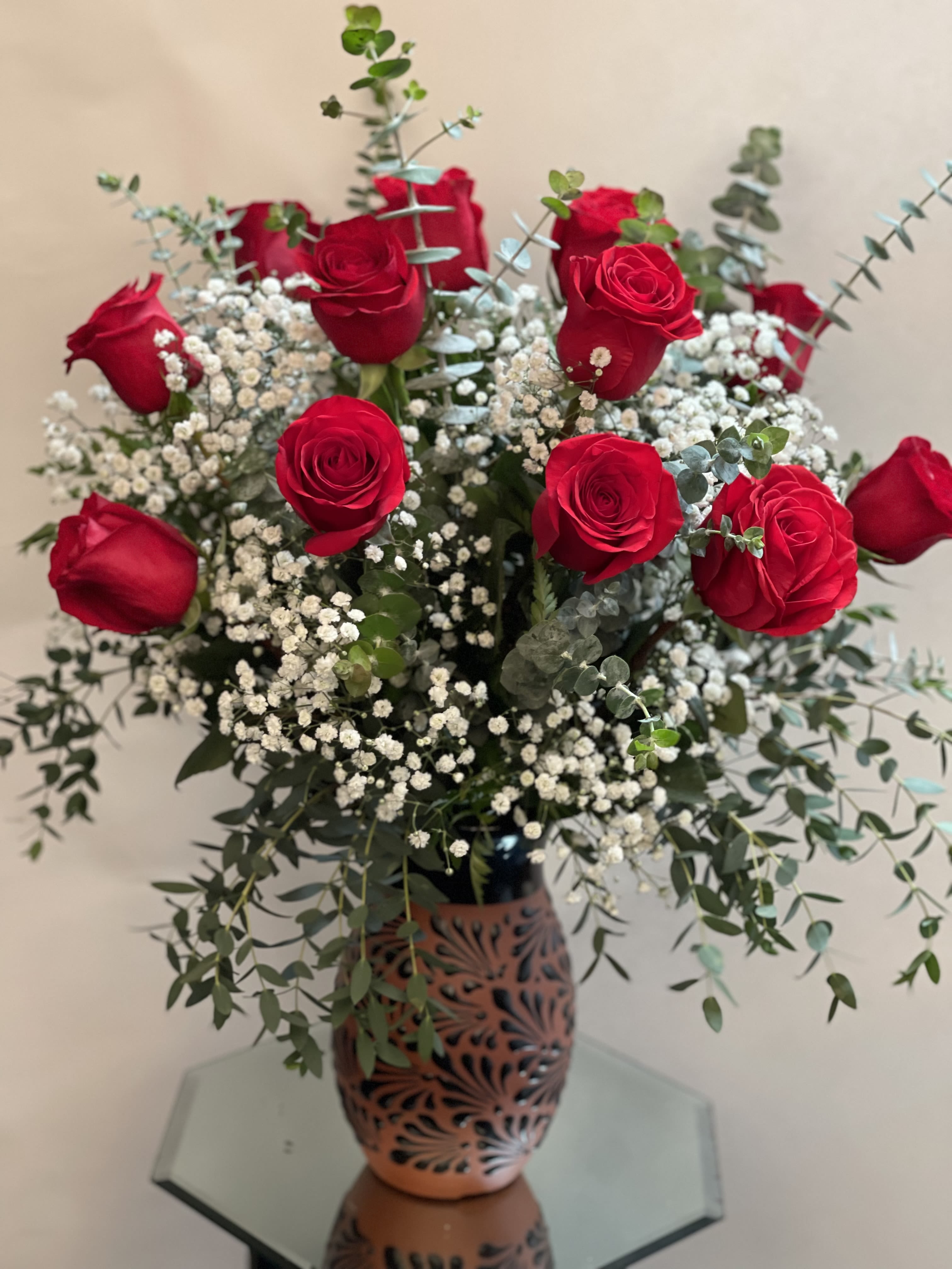 Red roses arranged in a decorative vase with baby's breath and eucalyptus