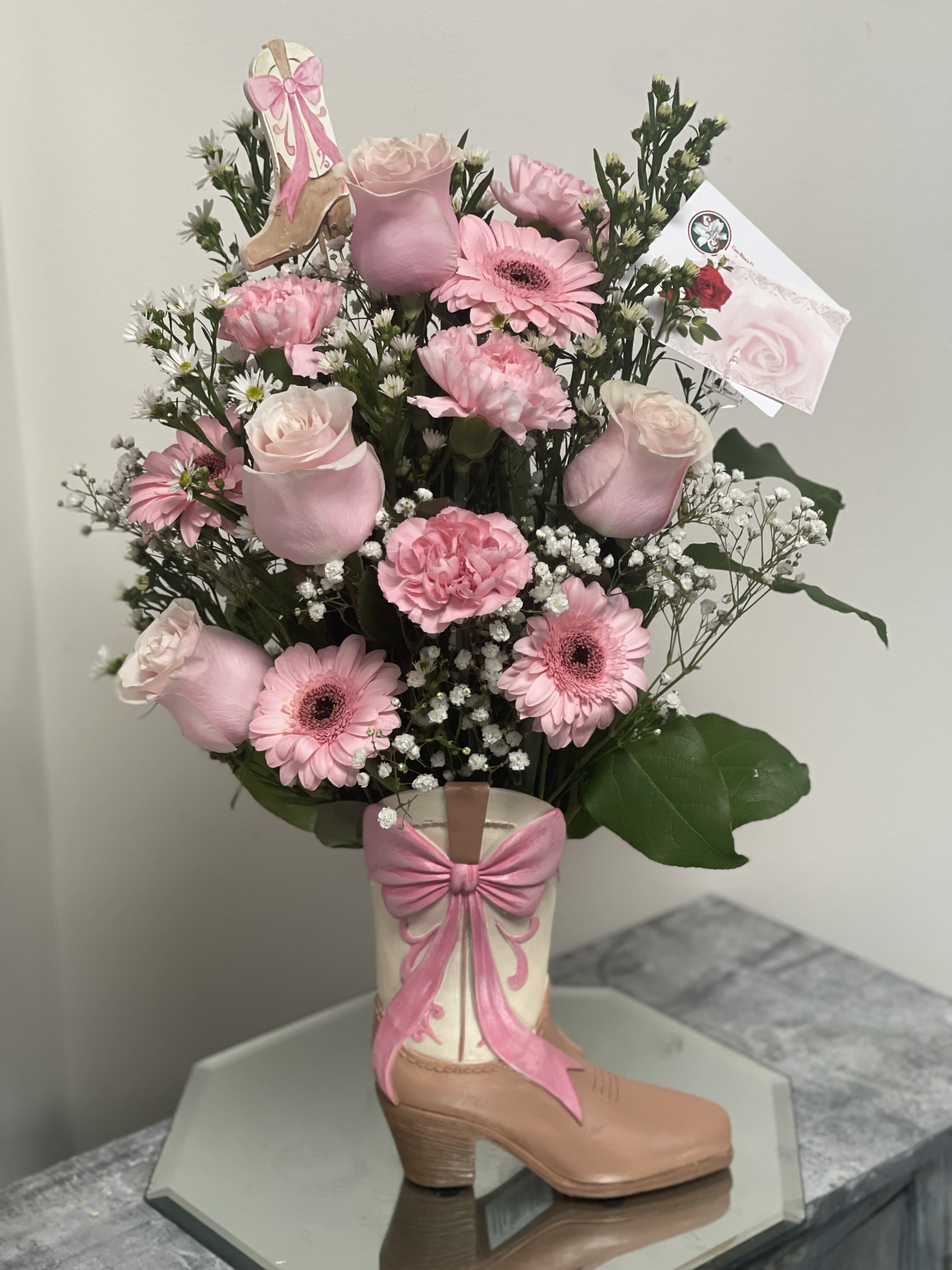 Pink flower arrangement in a decorative boot vase with a bow