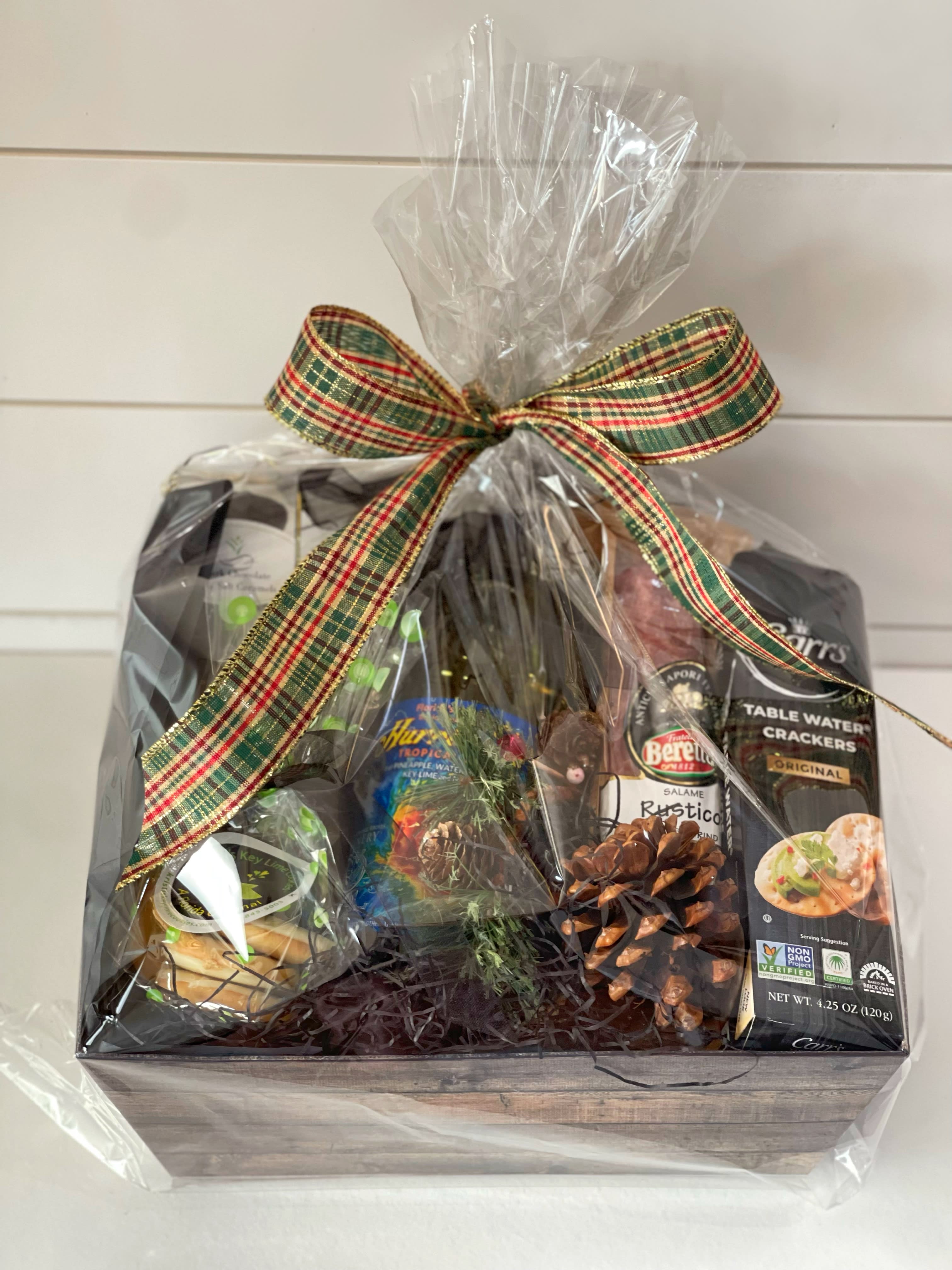 Gift basket with crackers, salami, and other packaged snacks tied with a plaid ribbon