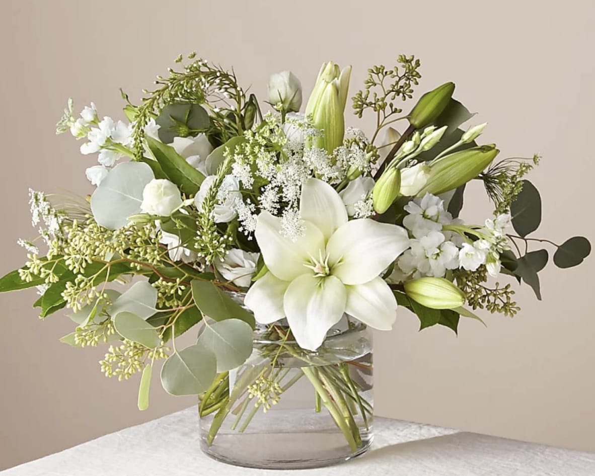 White lilies and greenery arranged in a clear glass vase