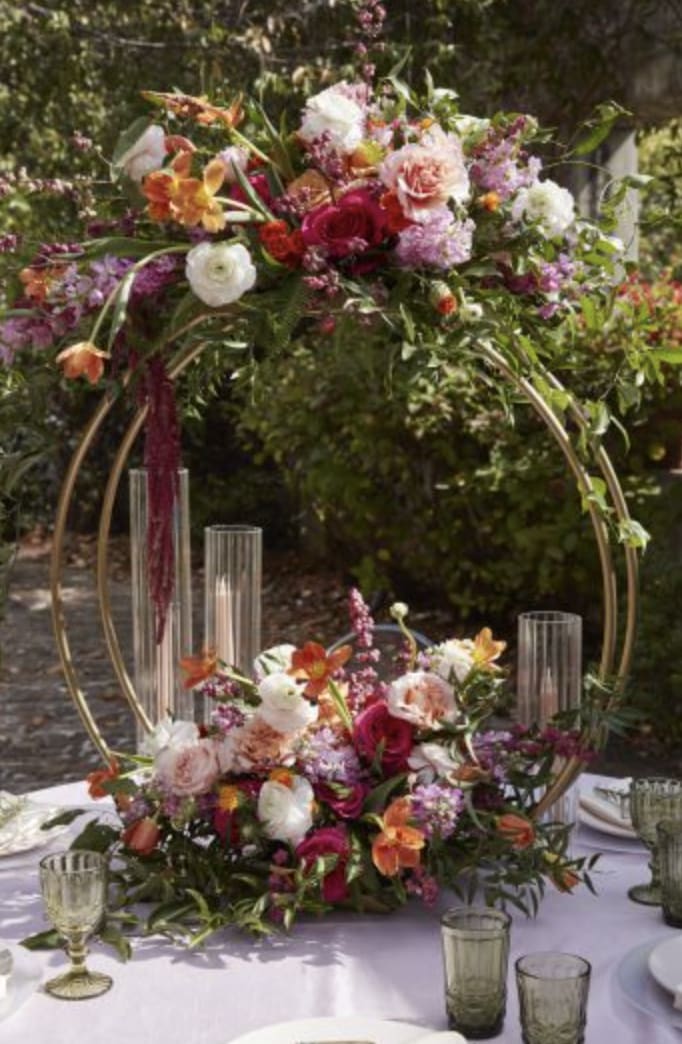 Two floral centerpieces on gold hoops with candles on a table