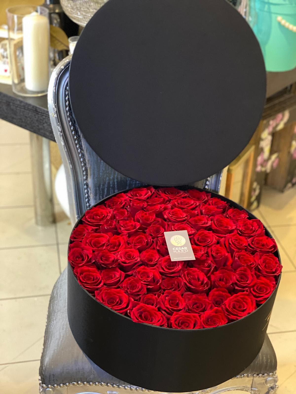 Parisian Hat Box - This elegant flower arrangement features stunning red roses artfully arranged in a chic black hat box. The full, lush bouquet creates a visual impact that radiates love is forever. Ideal for those seeking a unique and stylish gift, this red rose arrangement symbolizes passion, grace, and refined taste. Available in different colors per special request. 