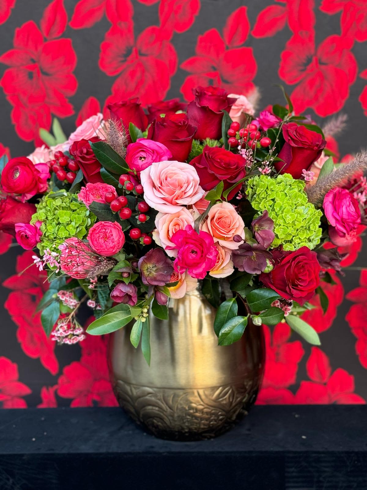 The Valentina! - An enchanting floral arrangement designed to evoke the essence of love. Set in a beautiful gold vase, to be used time and time again. This breathtaking display features a stunning collection of beautifully romantic flowers along with a mix of deep red and soft pink roses. The rich gold vase elevates the bouquet, accentuating the flowers’ vivid colors and delicate details. 