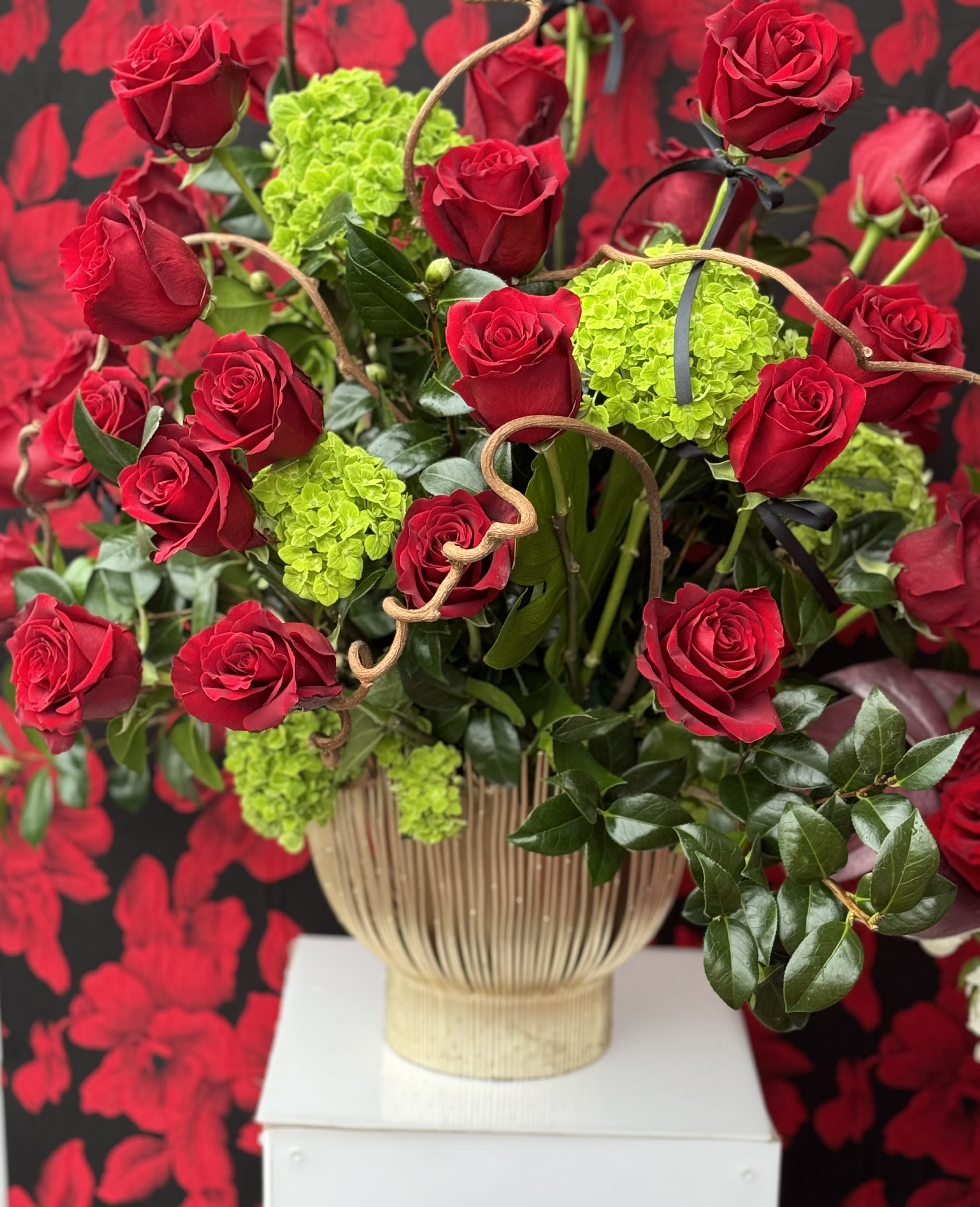 Garden of Eden - A captivating arrangement of rich red roses and soft hydrangeas, with delicate vines woven throughout. Set in a gold base with a natural twig-inspired design, this piece blends elegance with earthy charm, creating a striking and romantic display.