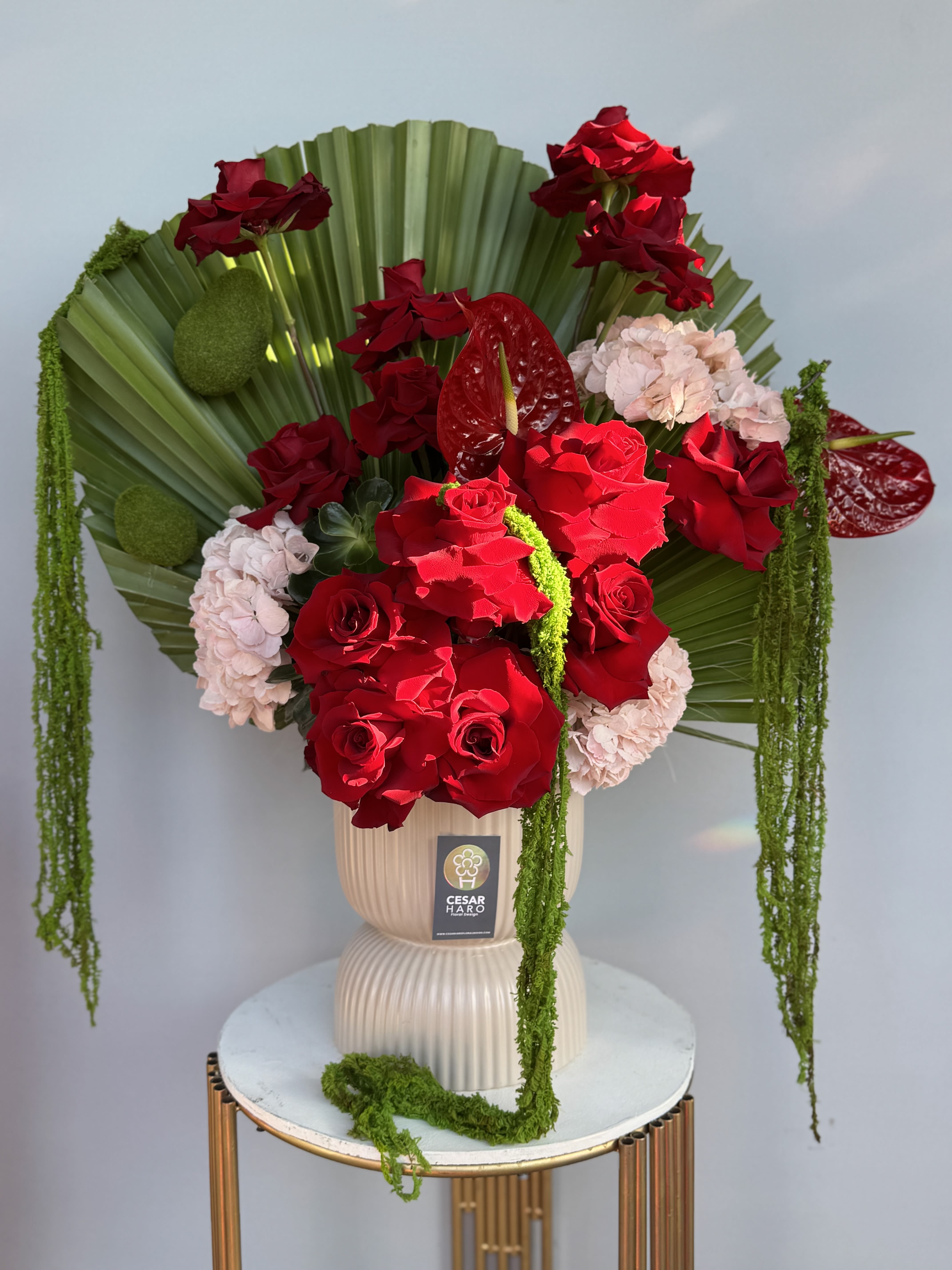 Enchanted Elegance - A dramatic white vase arrangement with palms, red roses, anthuriums, pink hydrangeas and elegant cascading greenery - instantly captivating and impossible not to fall in love with. 