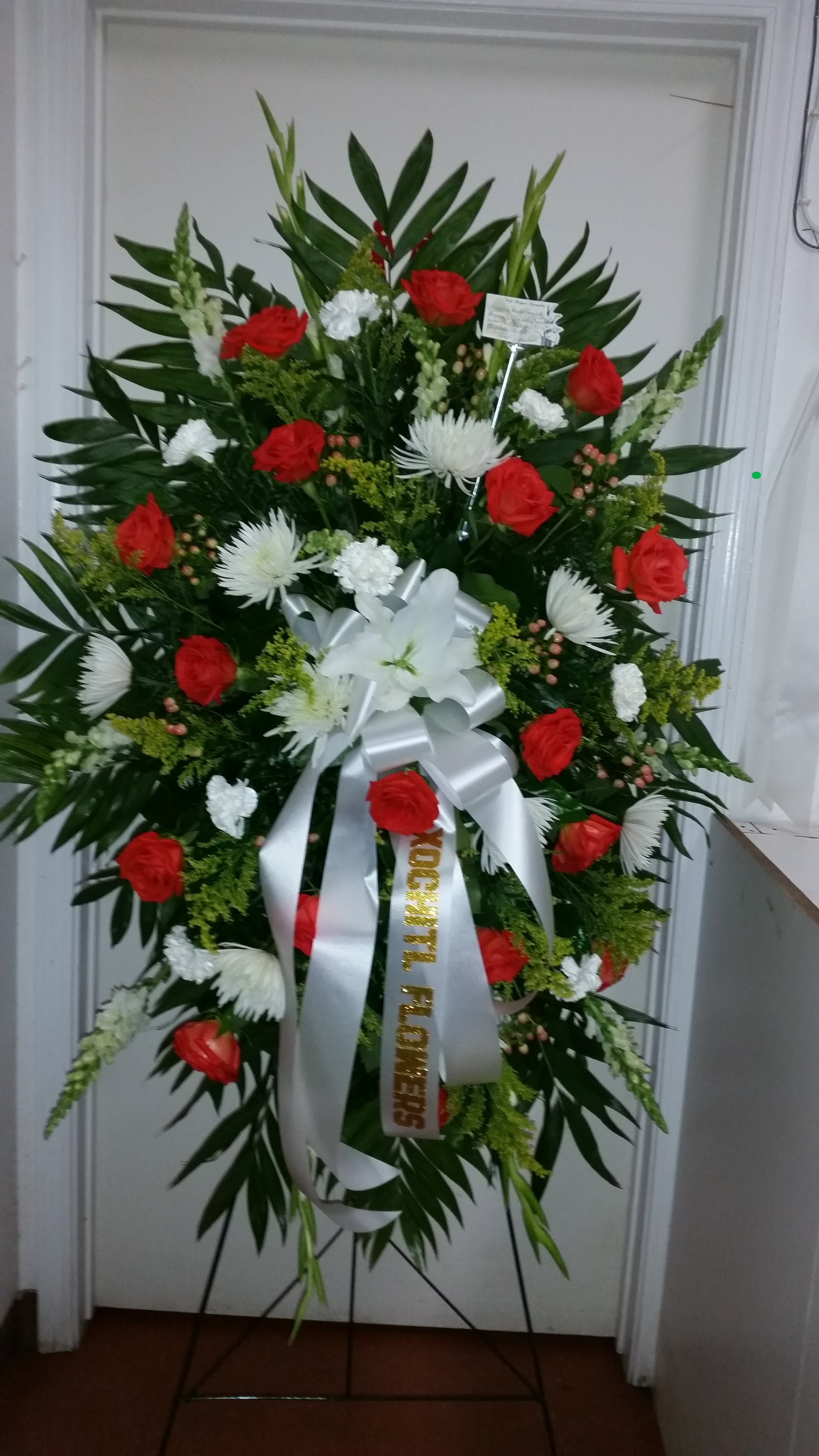 Standing floral wreath with red and white flowers on a metal easel