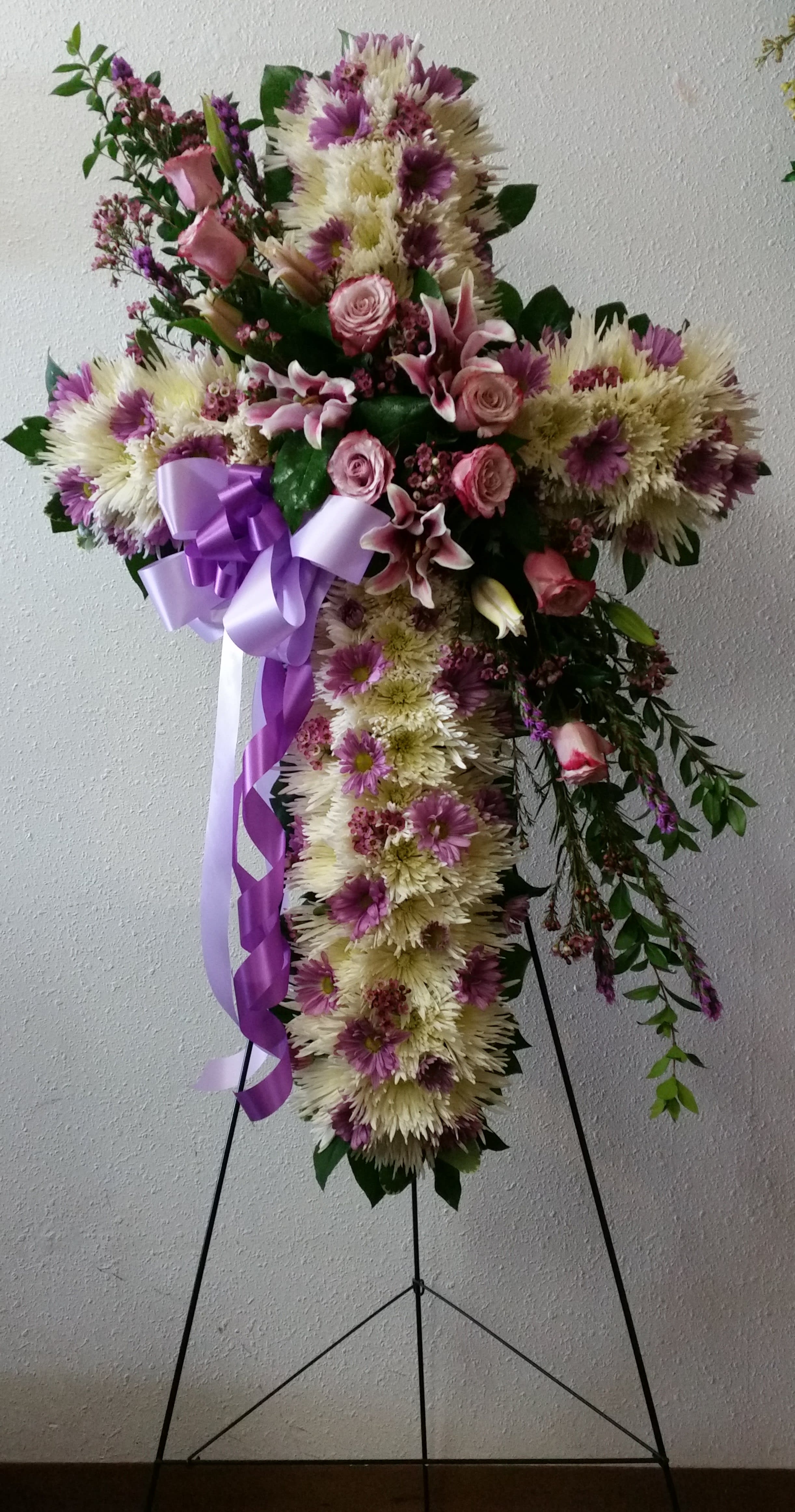 Cross-shaped floral standing spray with pink and white flowers and a purple ribbon