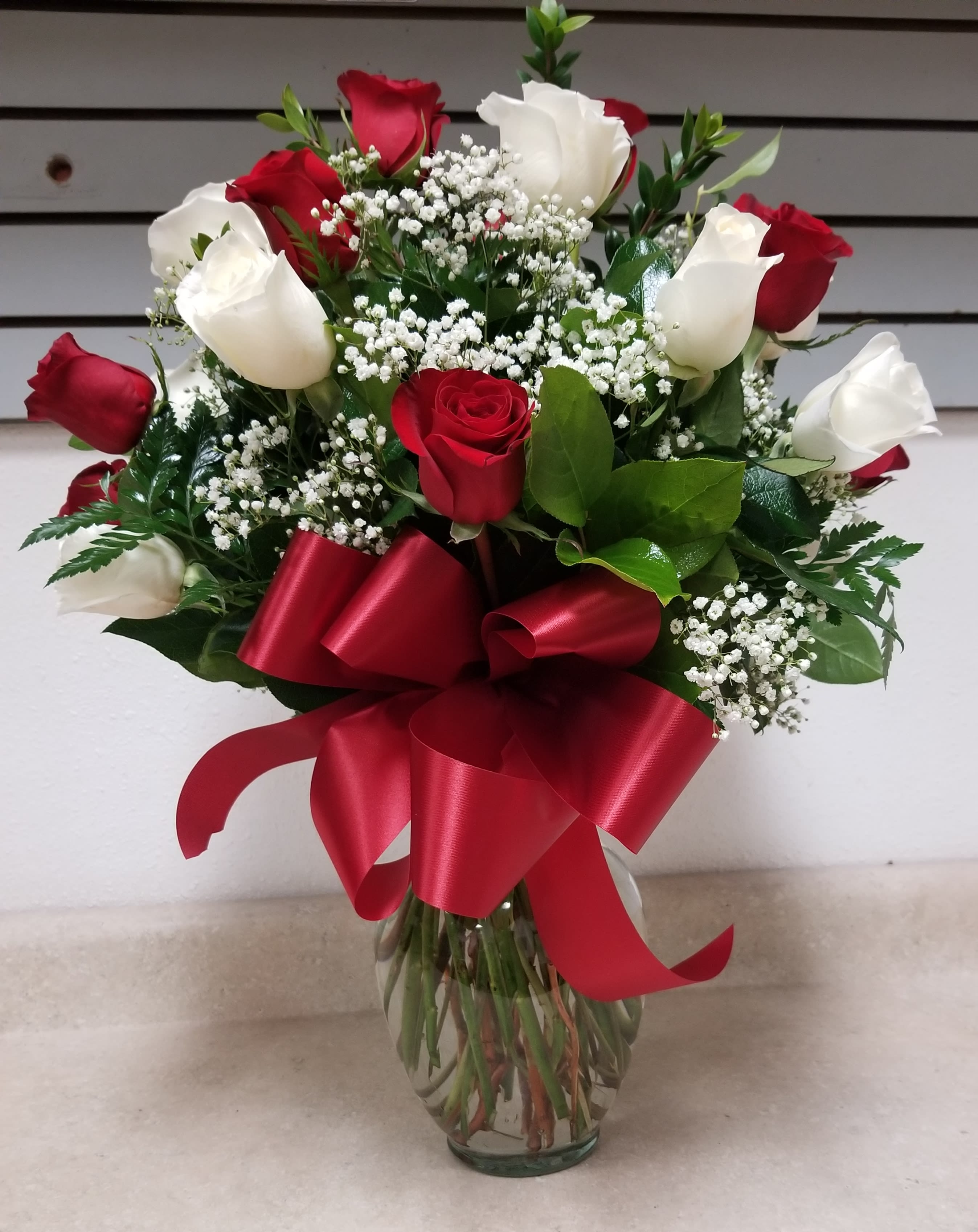 Red and white roses in a glass vase with a red ribbon