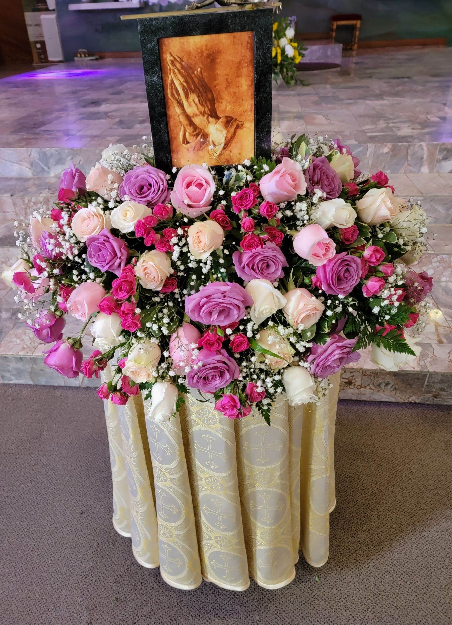 Large pink and white rose arrangement around a framed religious image