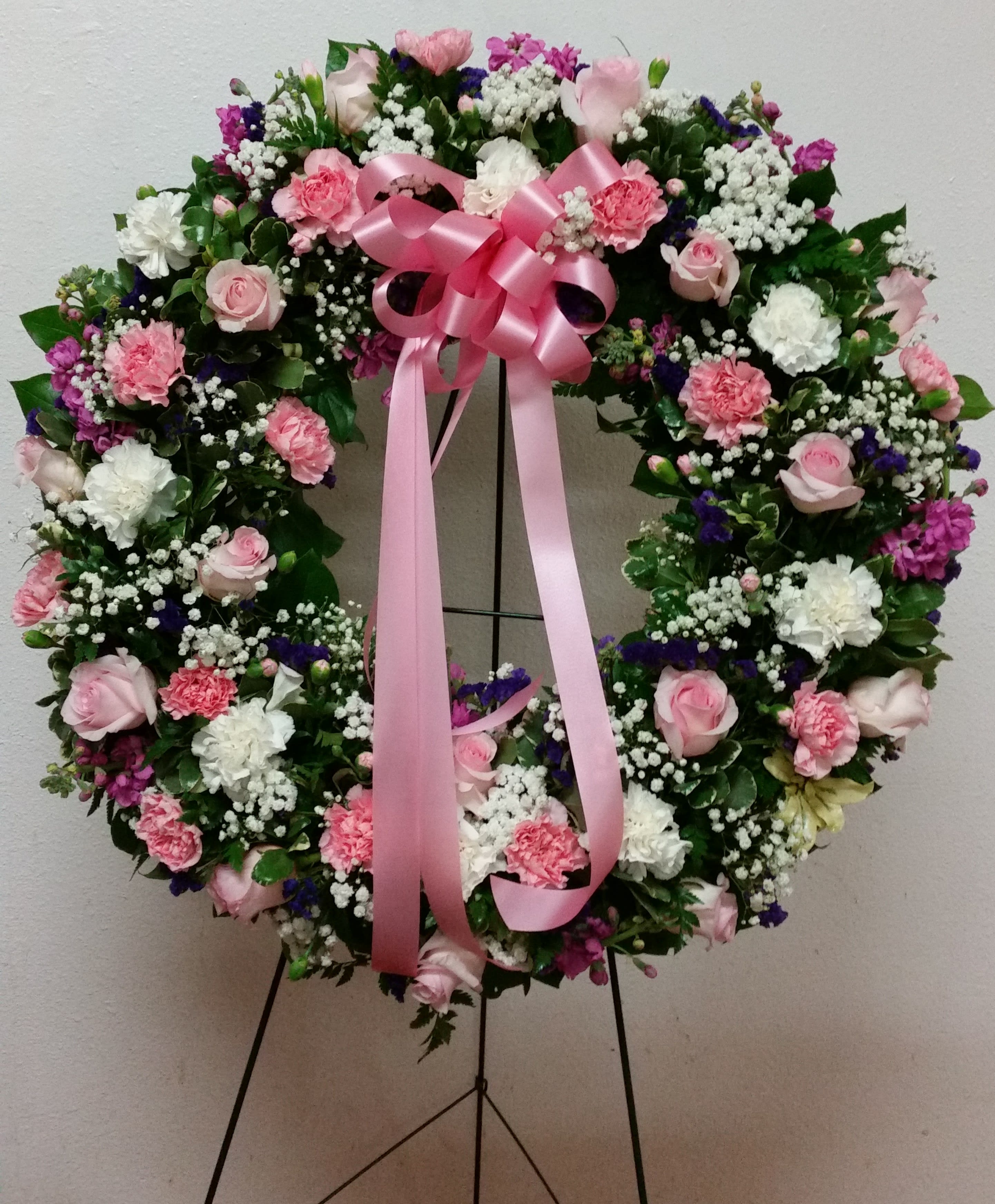 Heart-shaped floral wreath with pink ribbon on a stand