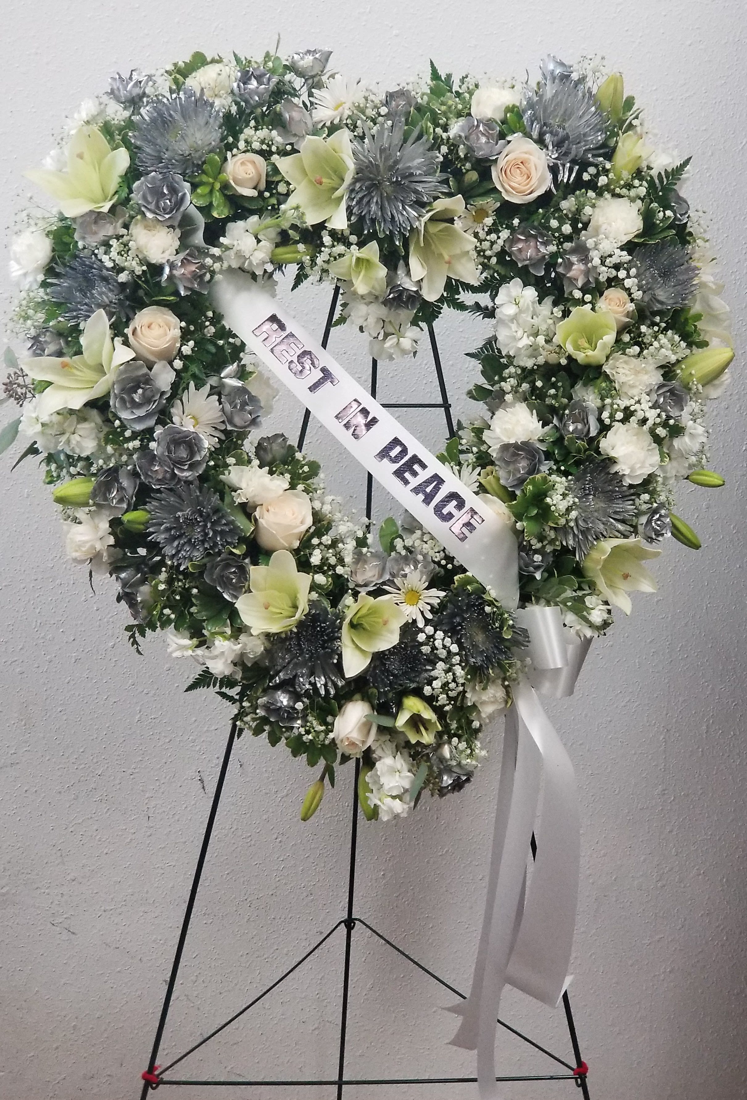 Heart-shaped funeral wreath with white and pale green flowers and a peace ribbon