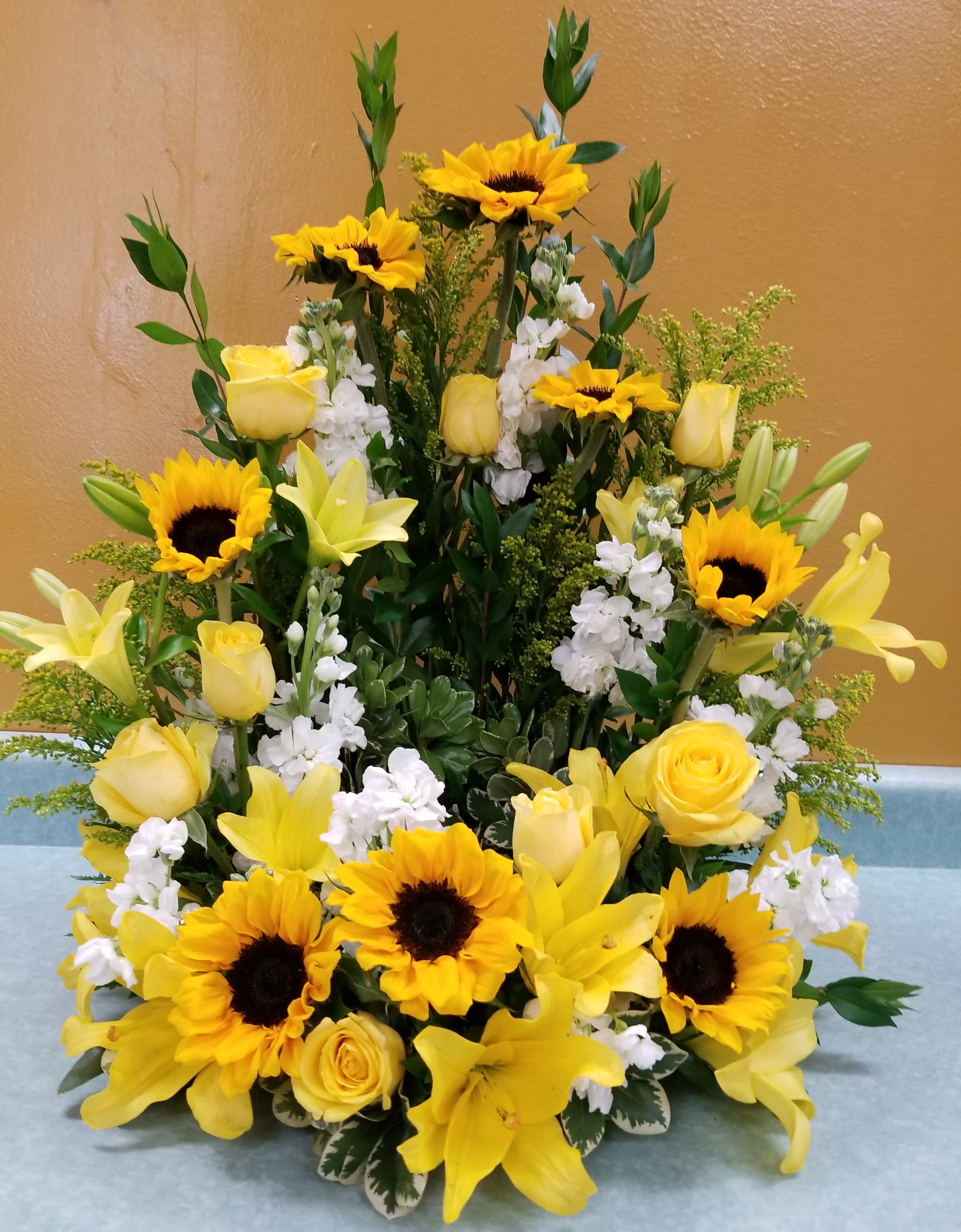 Yellow sunflowers, roses, and lilies arranged in a tall display