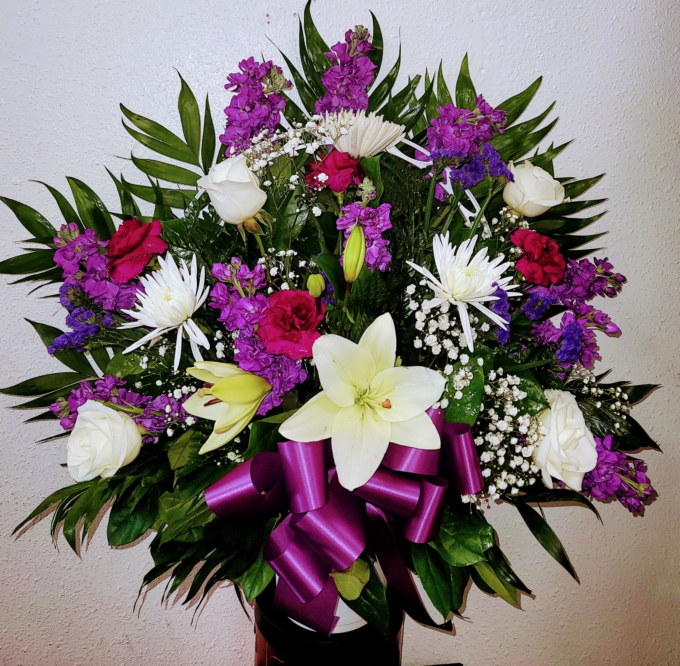 Bouquet of white lilies, roses, and purple flowers with a magenta ribbon