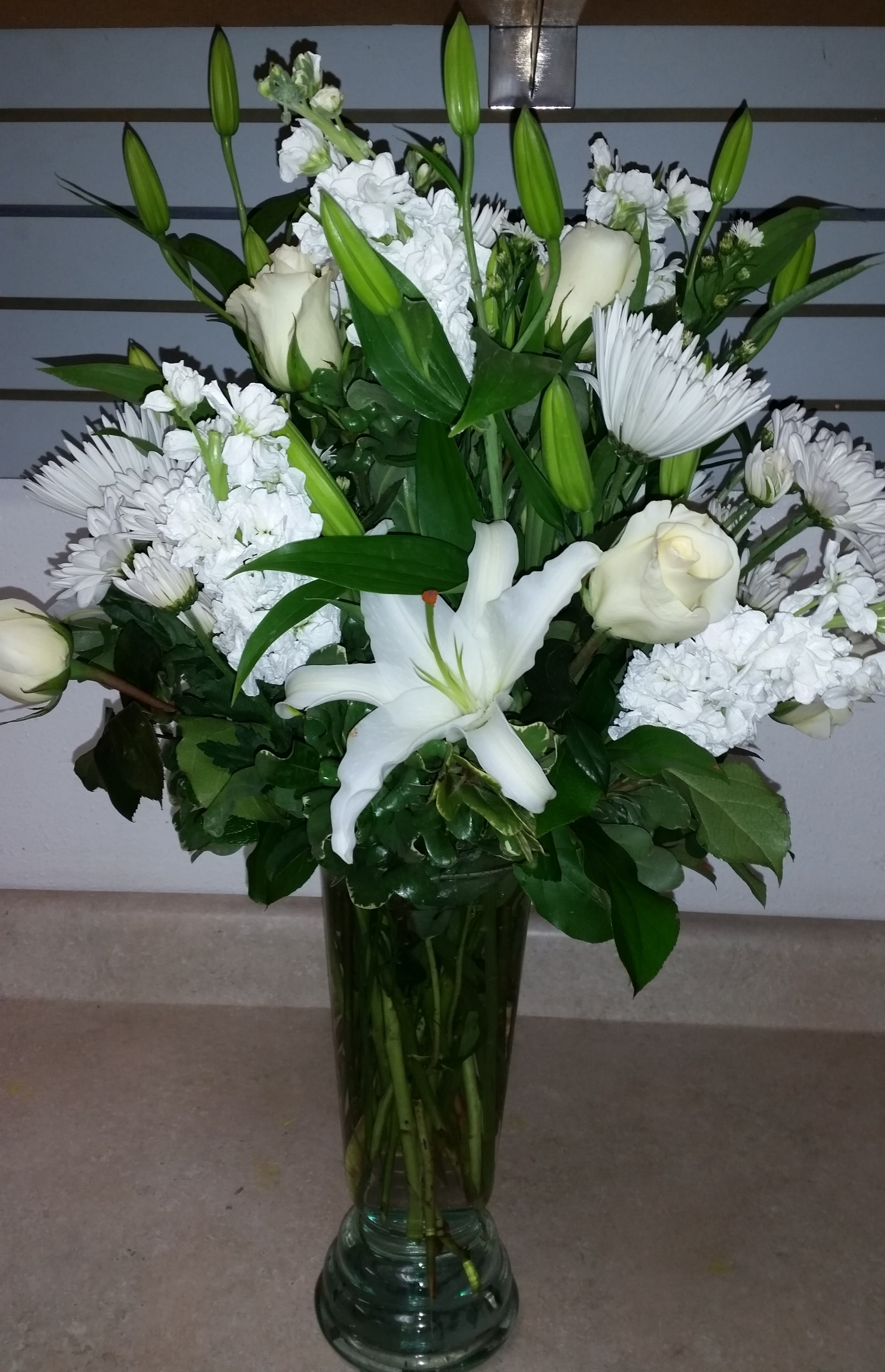 White lilies, roses, and daisies arranged in a tall glass vase