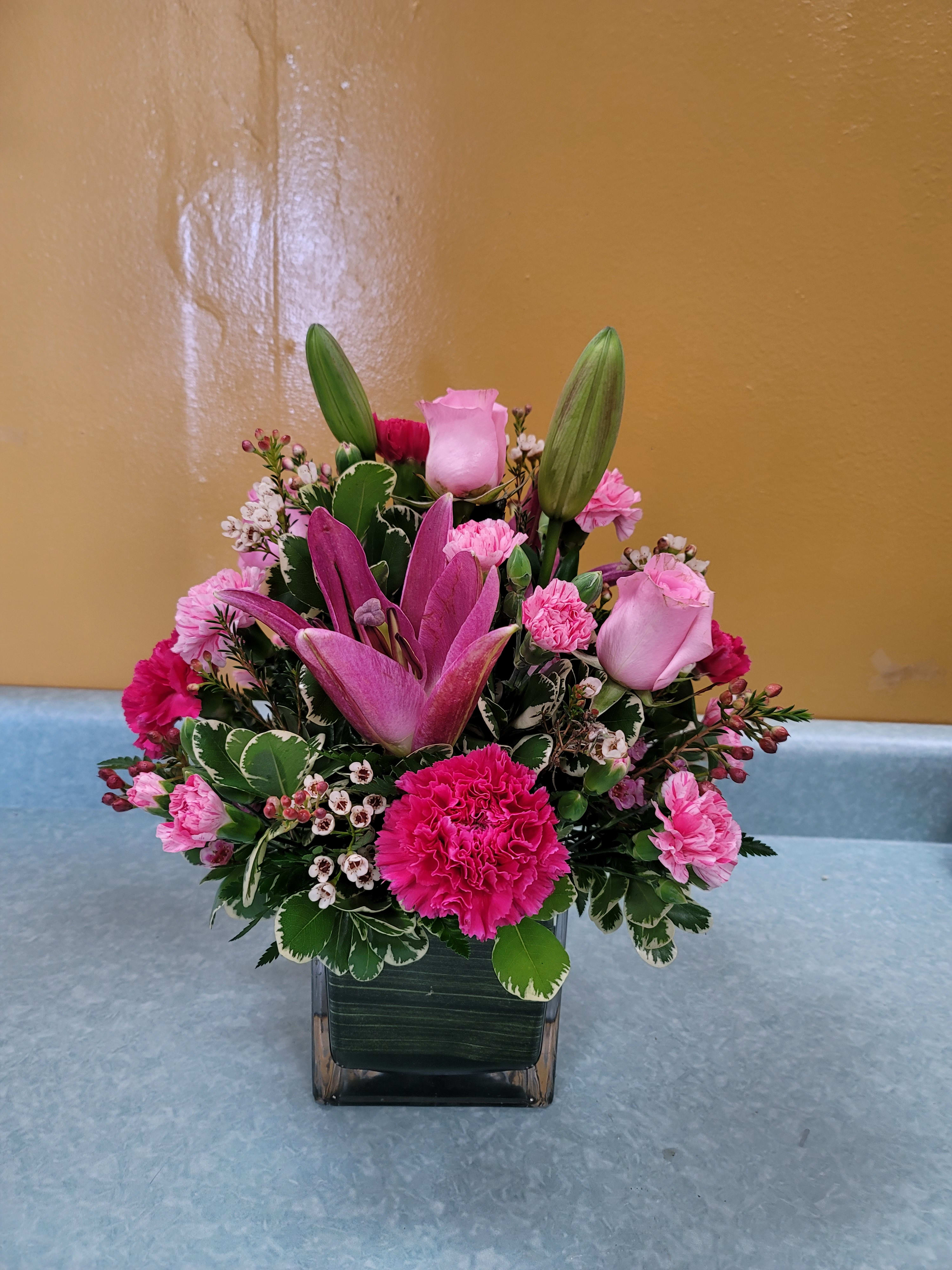 Pink lilies and roses arranged in a square glass vase