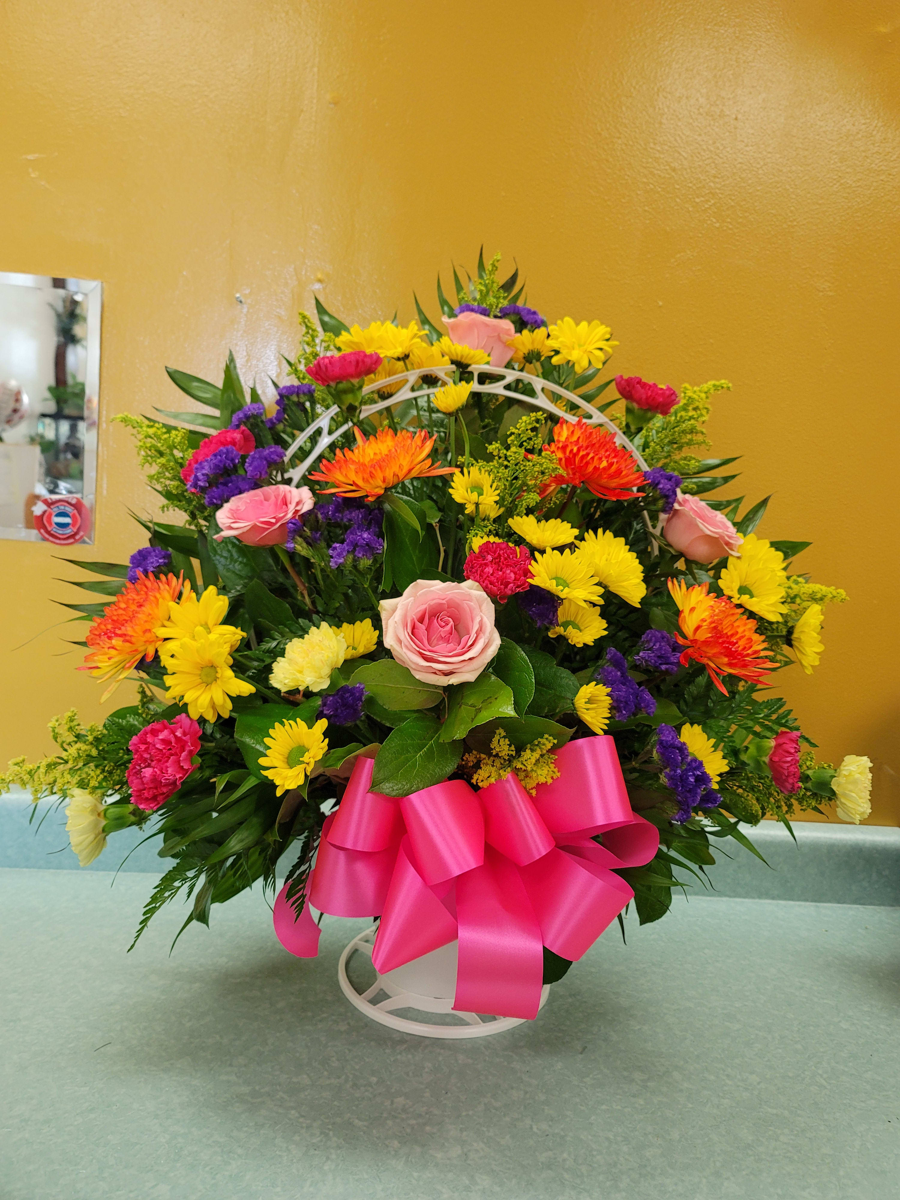 Colorful mixed flower arrangement with a pink ribbon on a white stand
