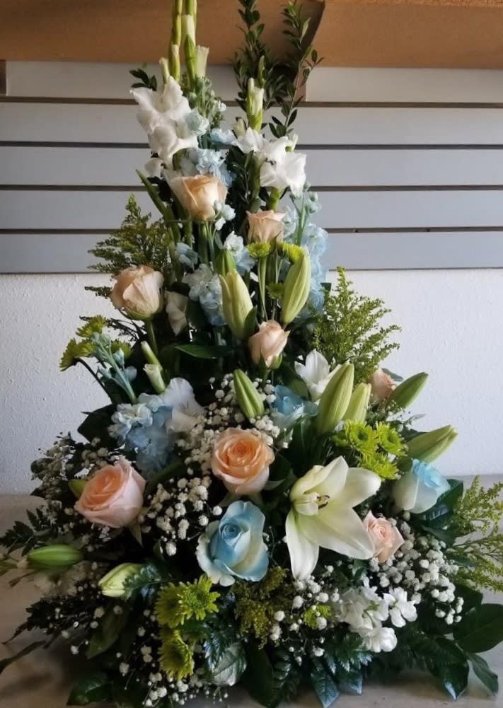 Tall floral spray with white lilies, pastel roses, and blue accents