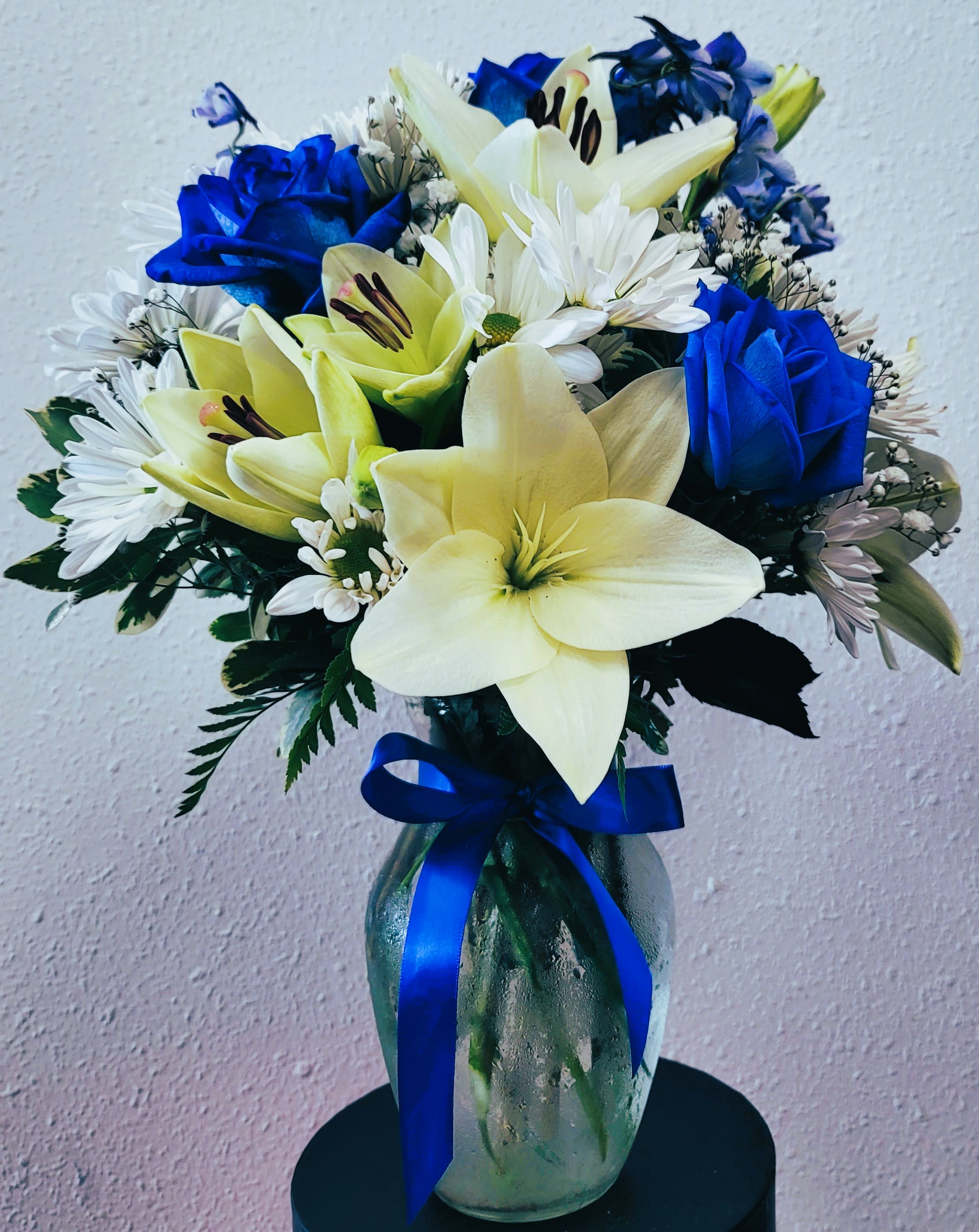 Bouquet of blue roses, white daisies, and pale lilies in a glass vase