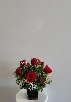 Red roses arranged in a square glass vase with white filler flowers