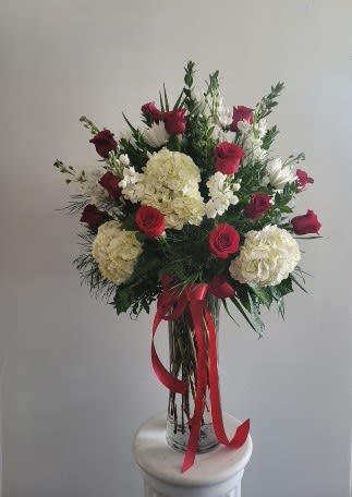 Tall bouquet of red roses and white hydrangeas in a glass vase with red ribbon