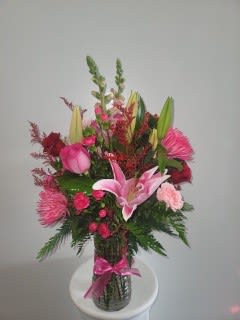 Pink and red floral arrangement in a glass vase with a pink ribbon